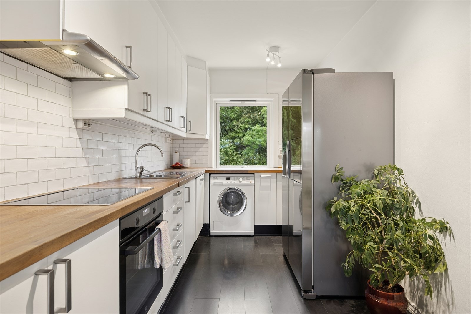 Et lyst kjøkken som gir et moderne og tidløst uttrykk med sine glatte, malte fronter og en benkeplate i heltre. Galleribilde