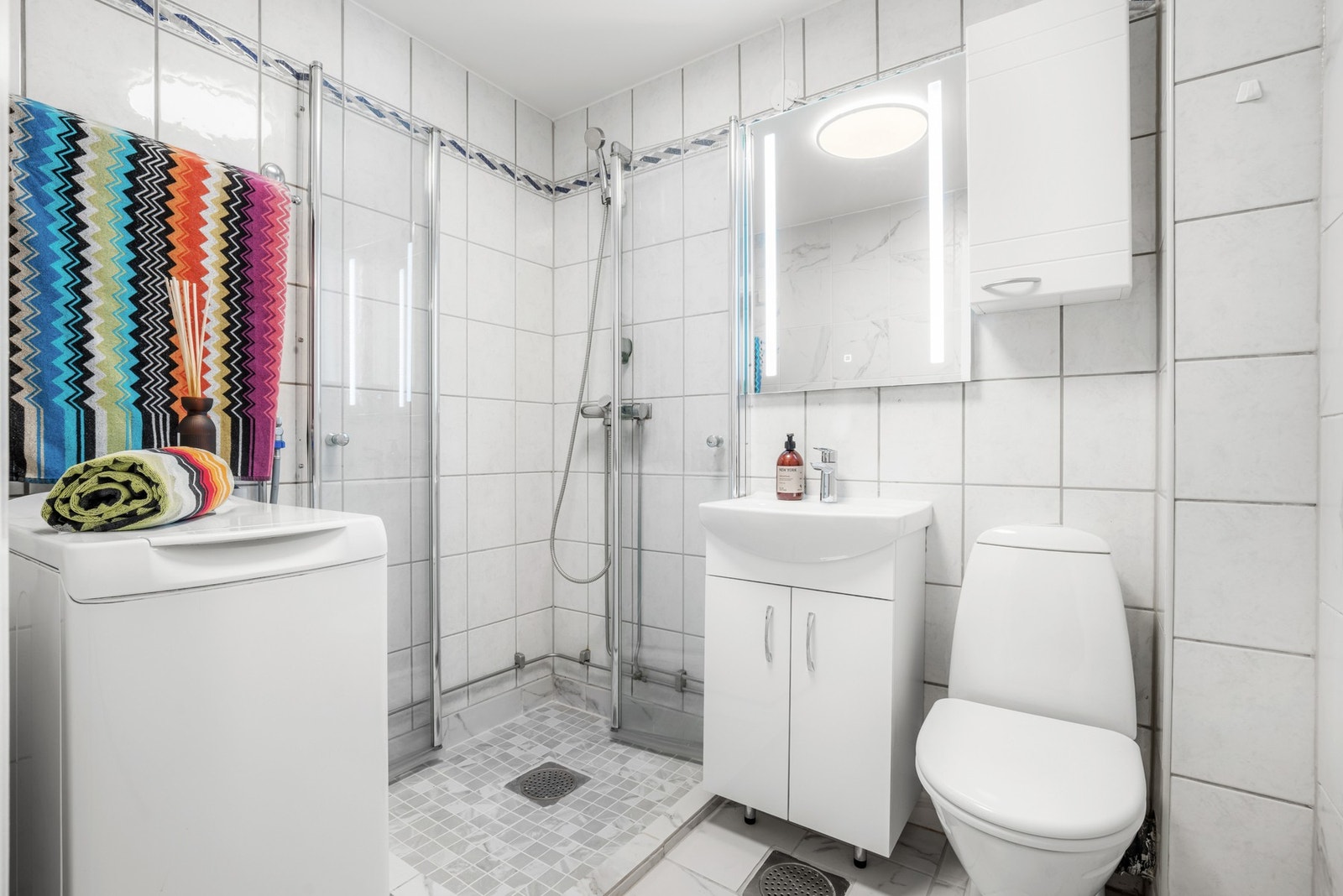 I tillegg er det lagt nye gulvfliser med opphevet gulv i dusjsonen og veggfliser på 2 stk vegger. Videre har badet et gulvmontert toalett, et dusjhjørne og opplegg for vaskemaskin. Galleribilde