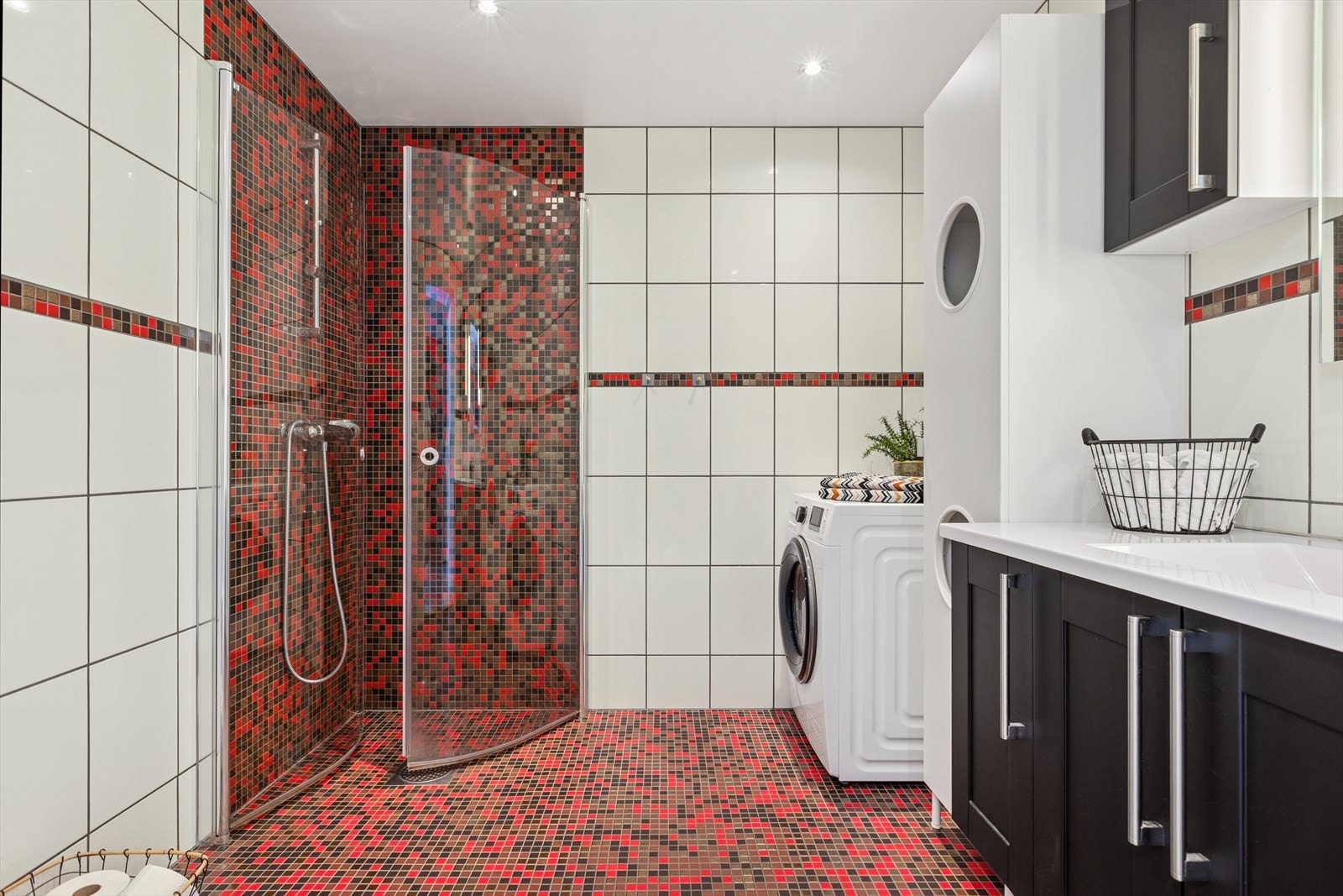 Rommet er innredet med vegghengt toalett, stilren sort baderomsinnredning med servant, og et dusjhjørne med glassvegger og veggmontert dusjgarnityr. Det er også tilrettelagt for vaskemaskin. Galleribilde