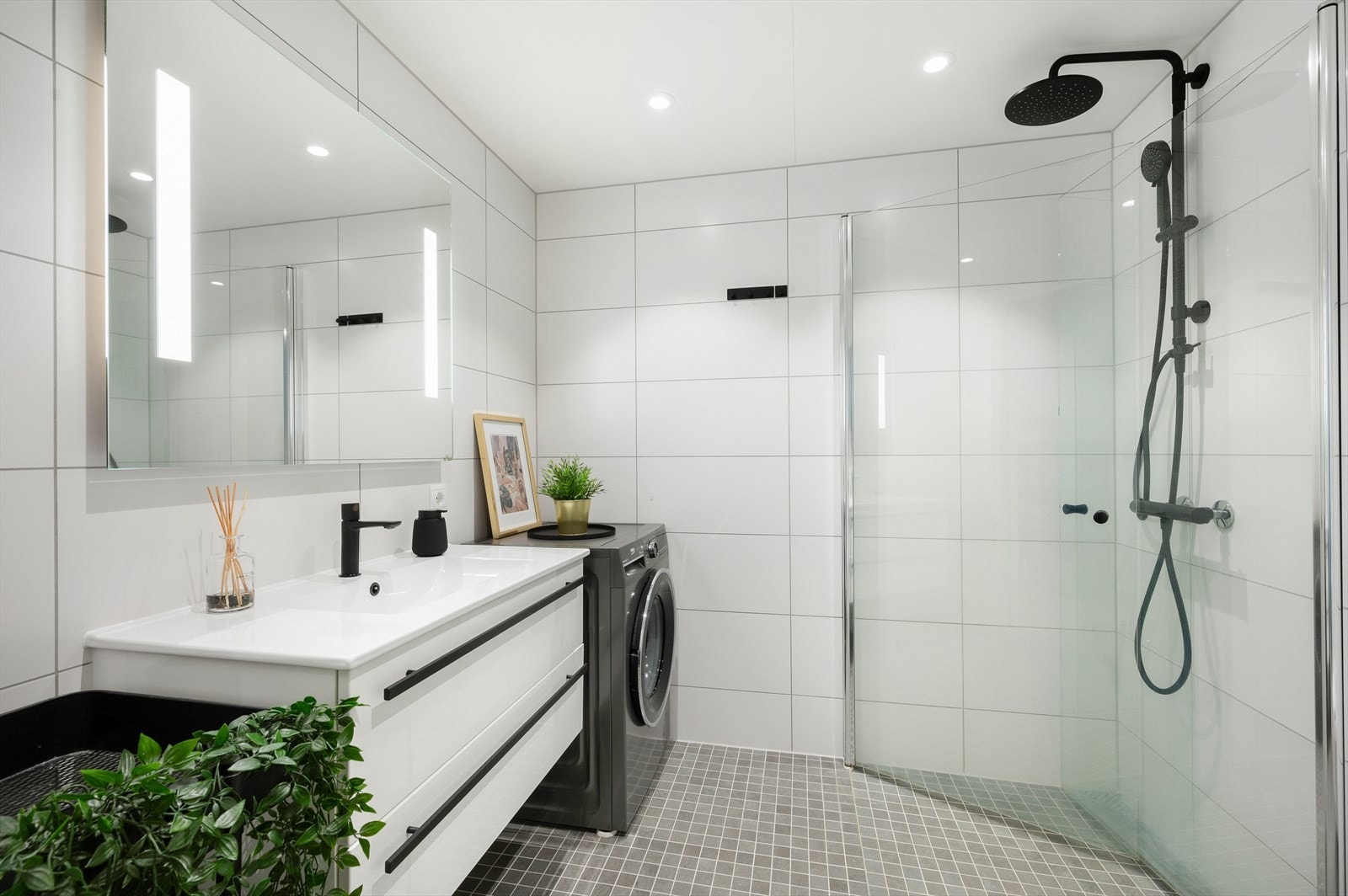 Delikat flislagt bad med lyse fliser, servant i skap, regndusj og vegghengt toalett. Galleribilde