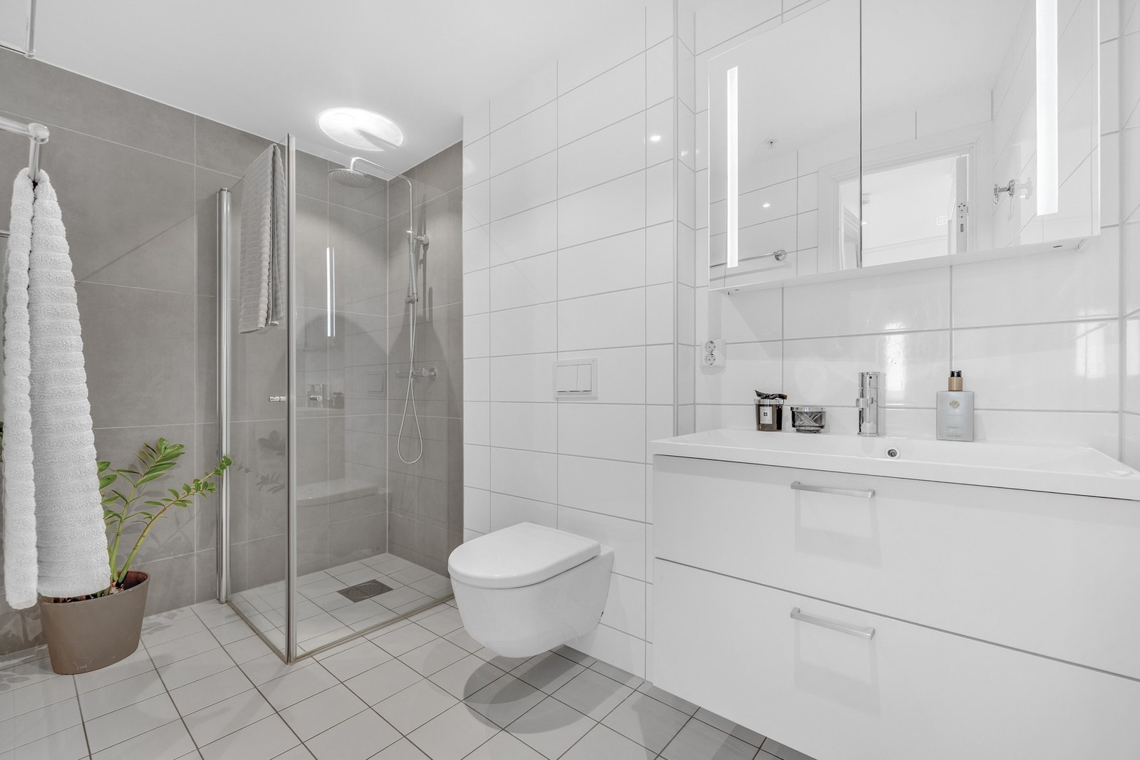 Lekkert og flislagt bad på 4,5 kvm med vegghengt WC, dusjhjørne med innfellbare dører og varmekabler i gulv. Godt med oppbevaring i både skuffer og speilskap. Galleribilde