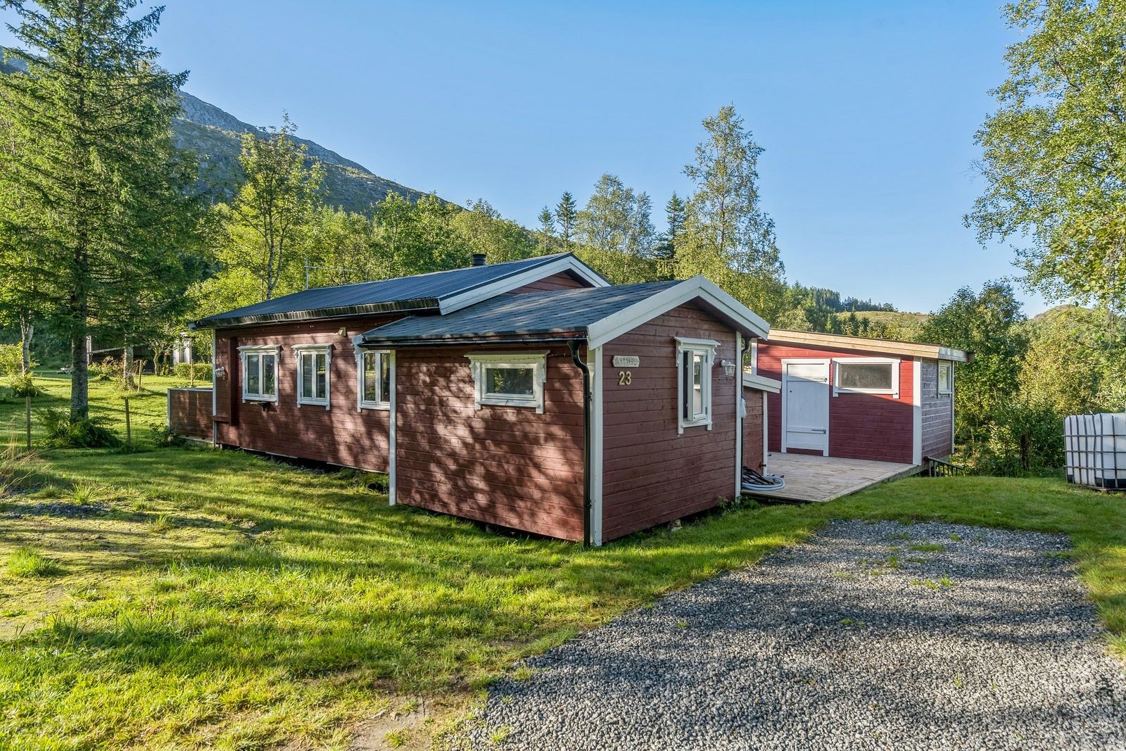 Gruset oppstillingsplass ved boligen. Tilbygget som sees som et lavt utstikk på terrassen er vannhuset der vanntank og pumpe er plassert (bygd i 2015), det er også strøm der inne og det er hengt opp en panelovn. Galleribilde