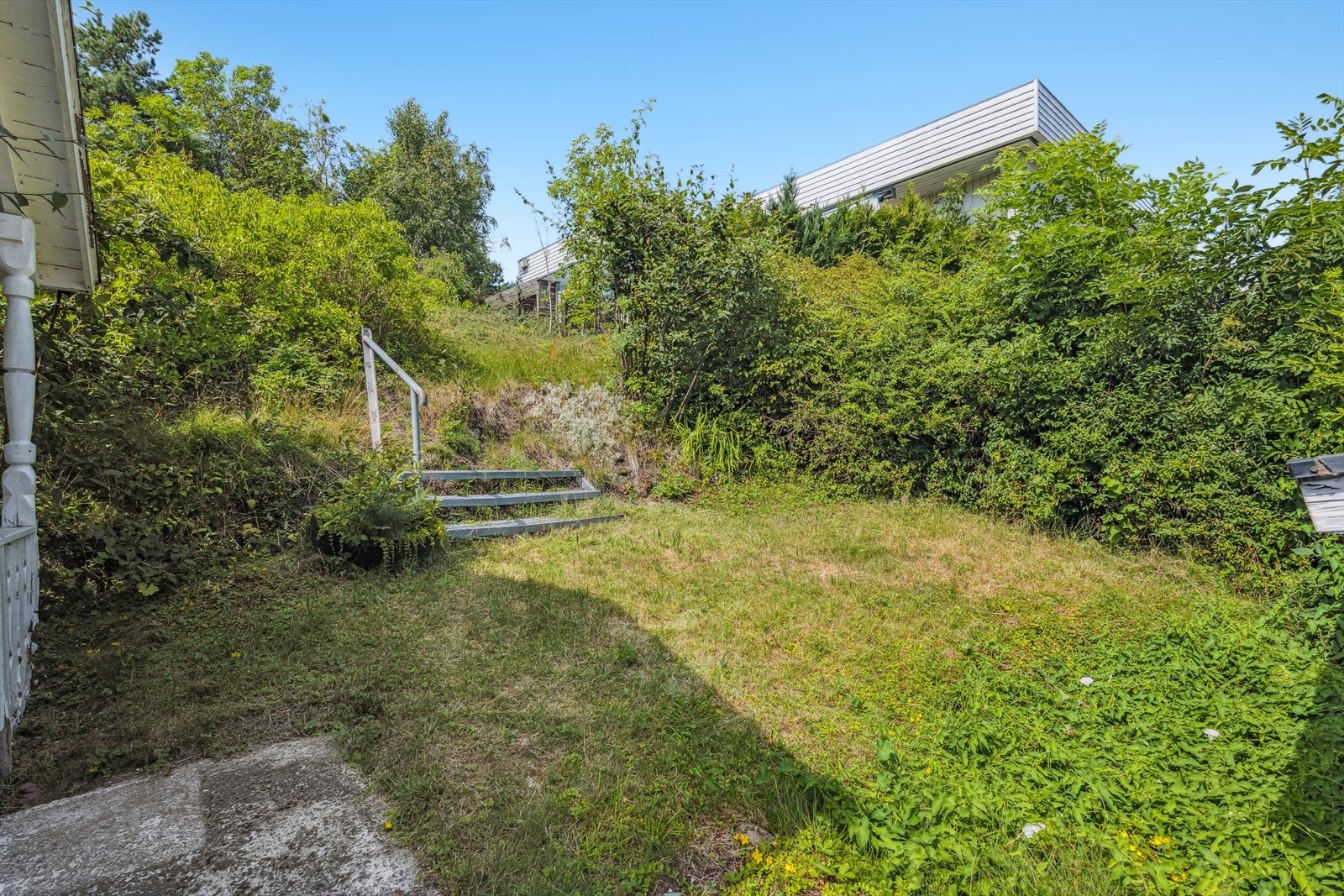 Solrik hage med naturpreg i skråmingen bak boligen. Galleribilde