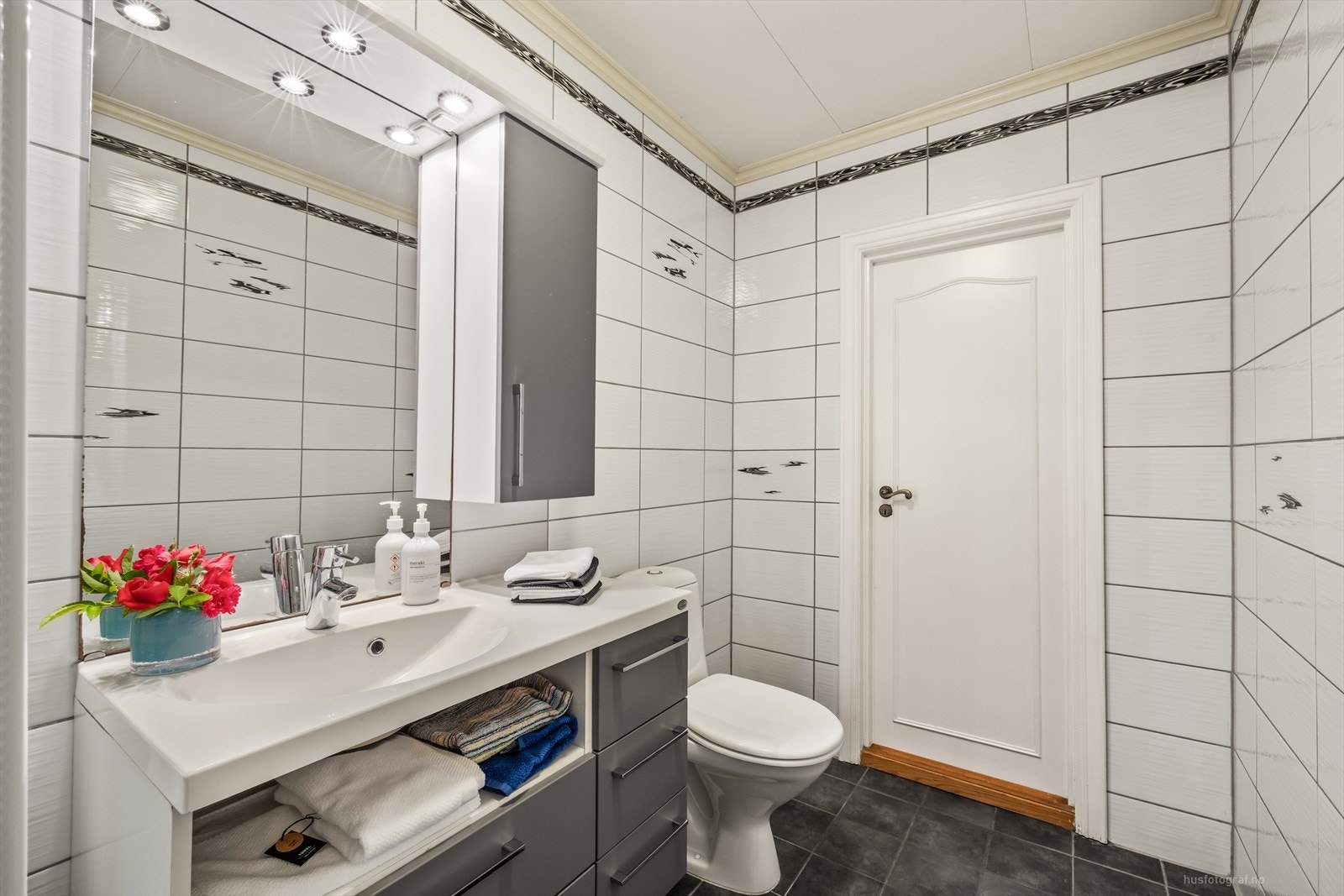 Badet inneholder dusjkabinett, toalett og servant med underskap. Spotter over speil. Galleribilde