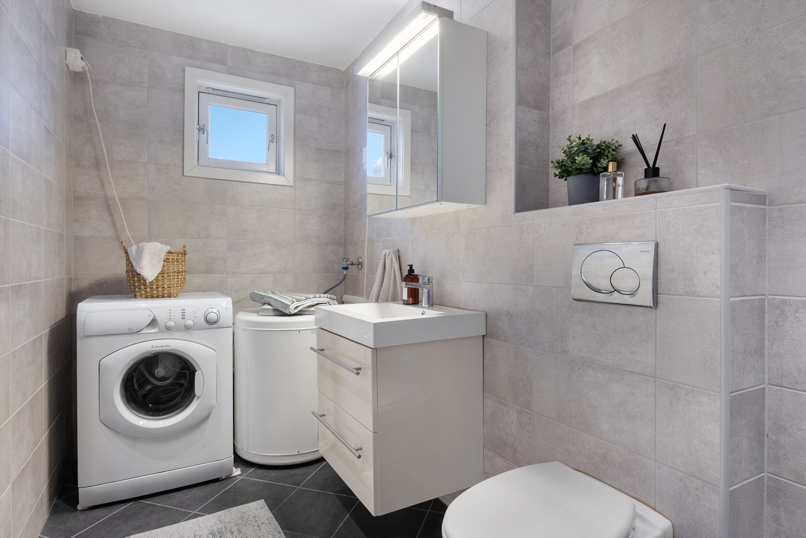 Badet er utstyrt med servantmøbel, speilskap med belysning, vegghengt toalett, innfelbart dusjhjørne i glass, dusjgarnityr, opplegg for vaskemaskin, varmtvannstank og avtrekksventil i vegg Galleribilde