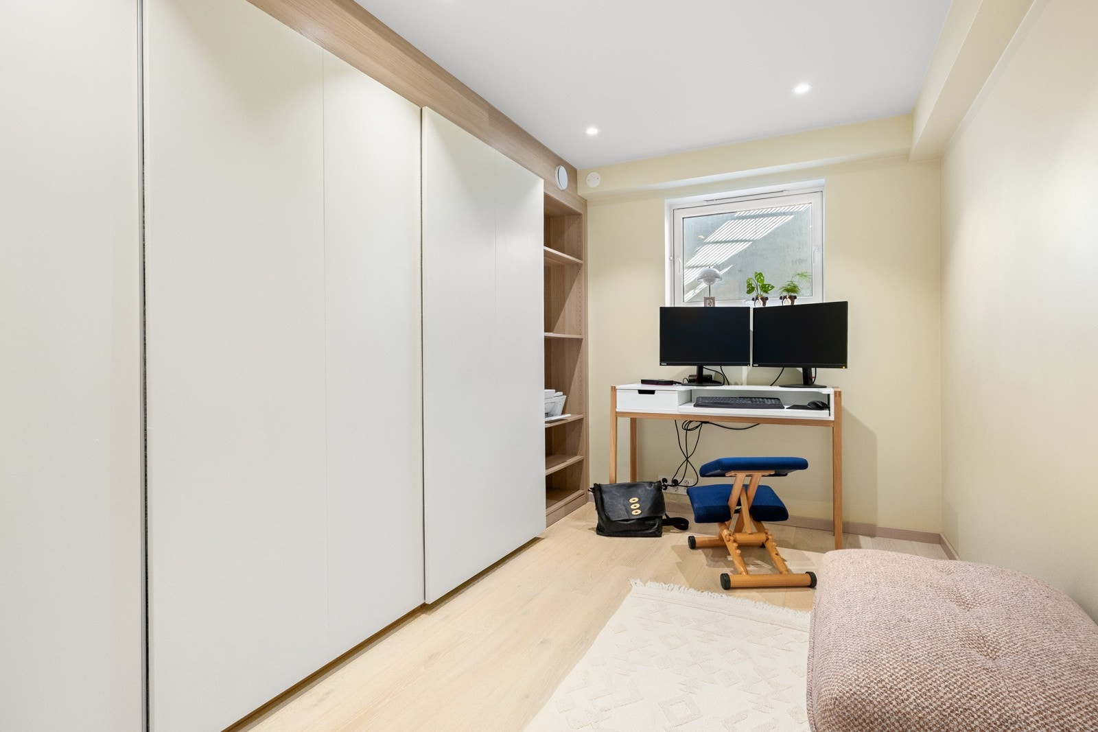 Et kontor i kjelleren er innredet med en stor skyvedørsgarderobe som har hvite fronter og innmat i eikelaminat. Galleribilde