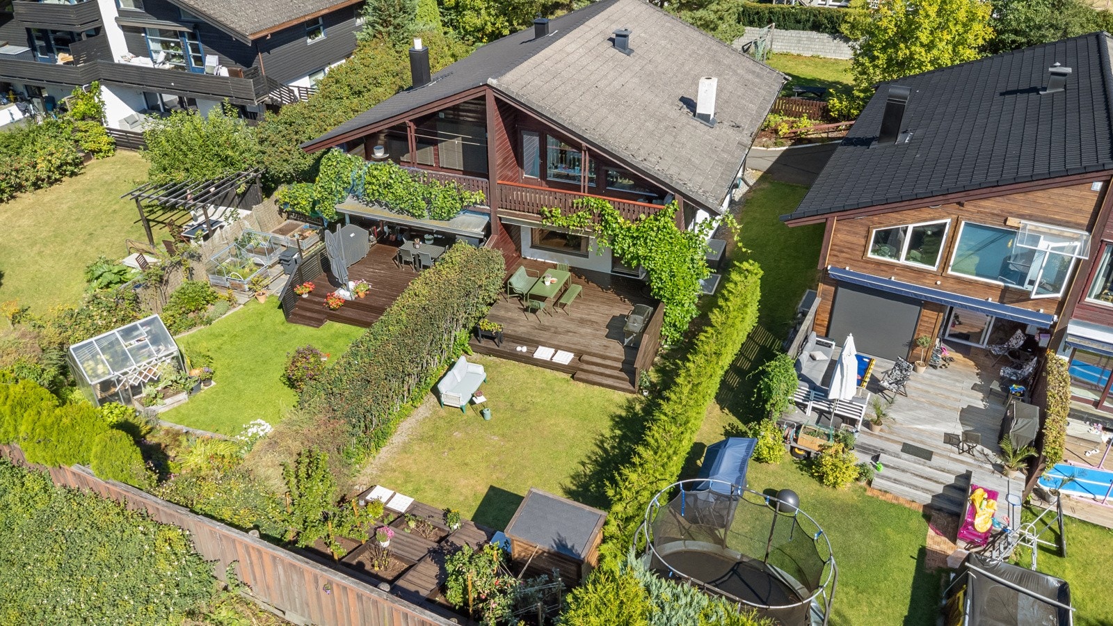 Hageoasen ligger usjenert og solrikt, omkranset av hekk, blomsterbed, og klatreplanter som slynger seg opp husveggen. Galleribilde