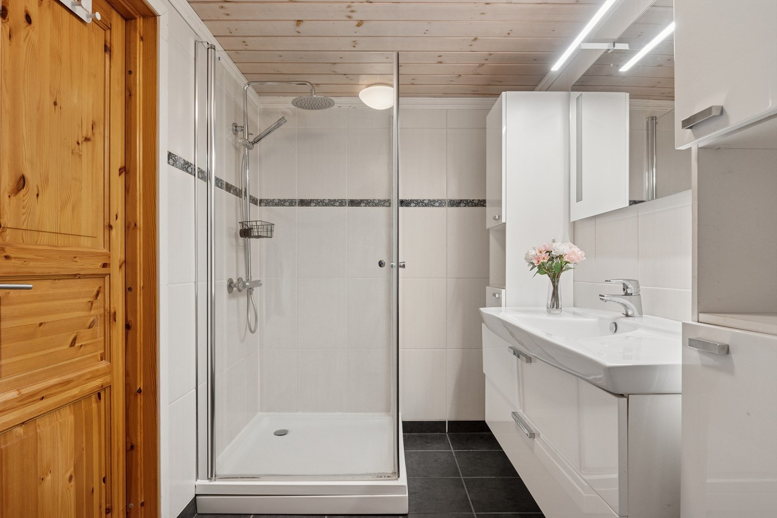 Baderommet er innredet med dusjhjørne, servant med tilhørende skap og toalett Galleribilde