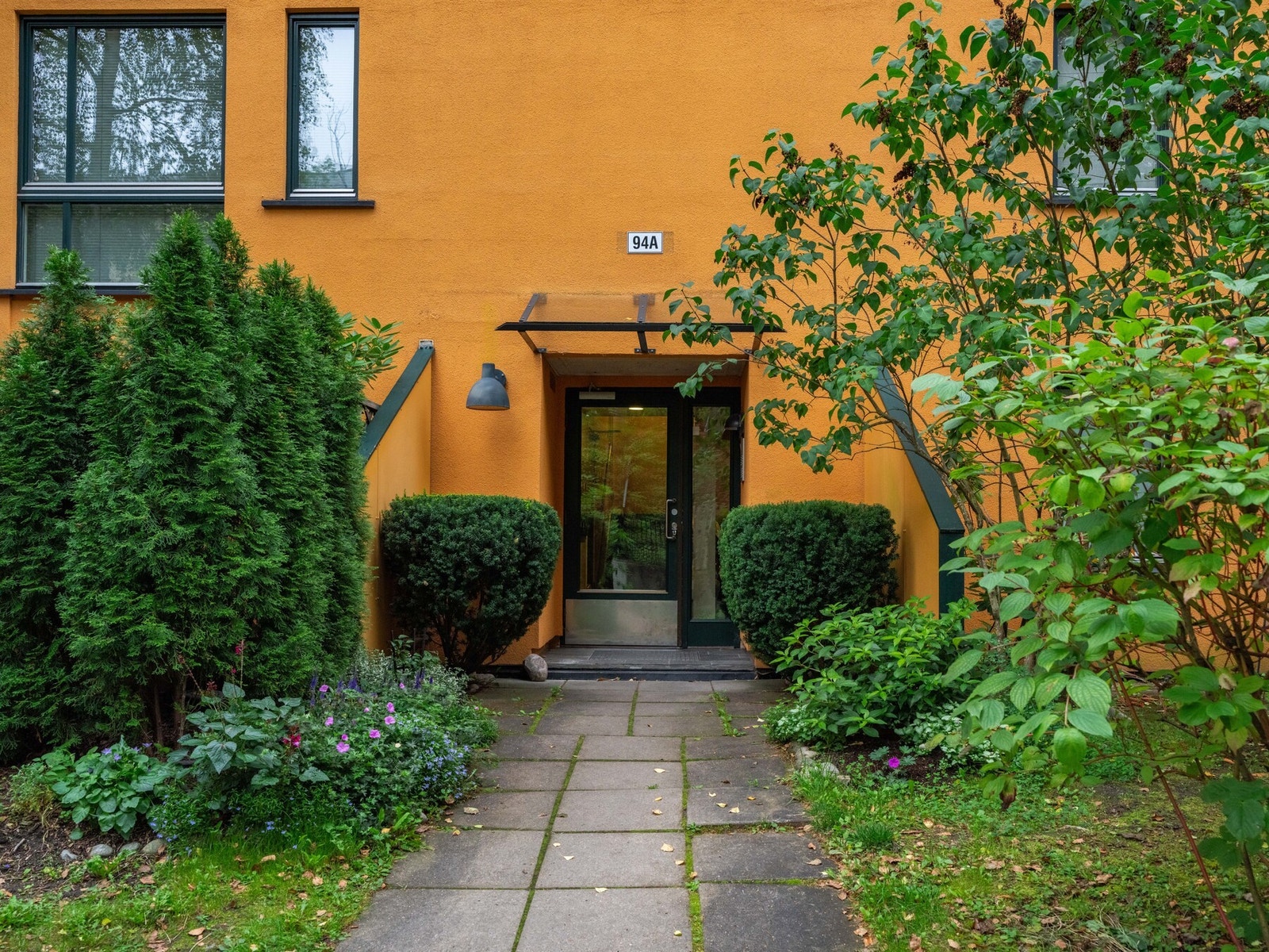 Inngangspartiet er omkranset av grønne trær og hyggelig beplantning. Galleribilde