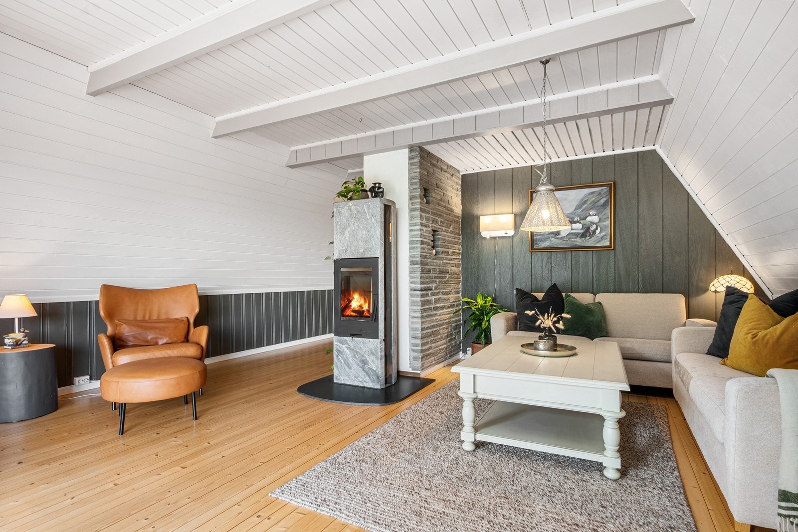 Stuen har heltre gulv, panel på vegger og en flott klebersteinspeis er plassert midt i rommet. Her er det plass til sofagruppe, lesekrok og TV-løsning. Galleribilde