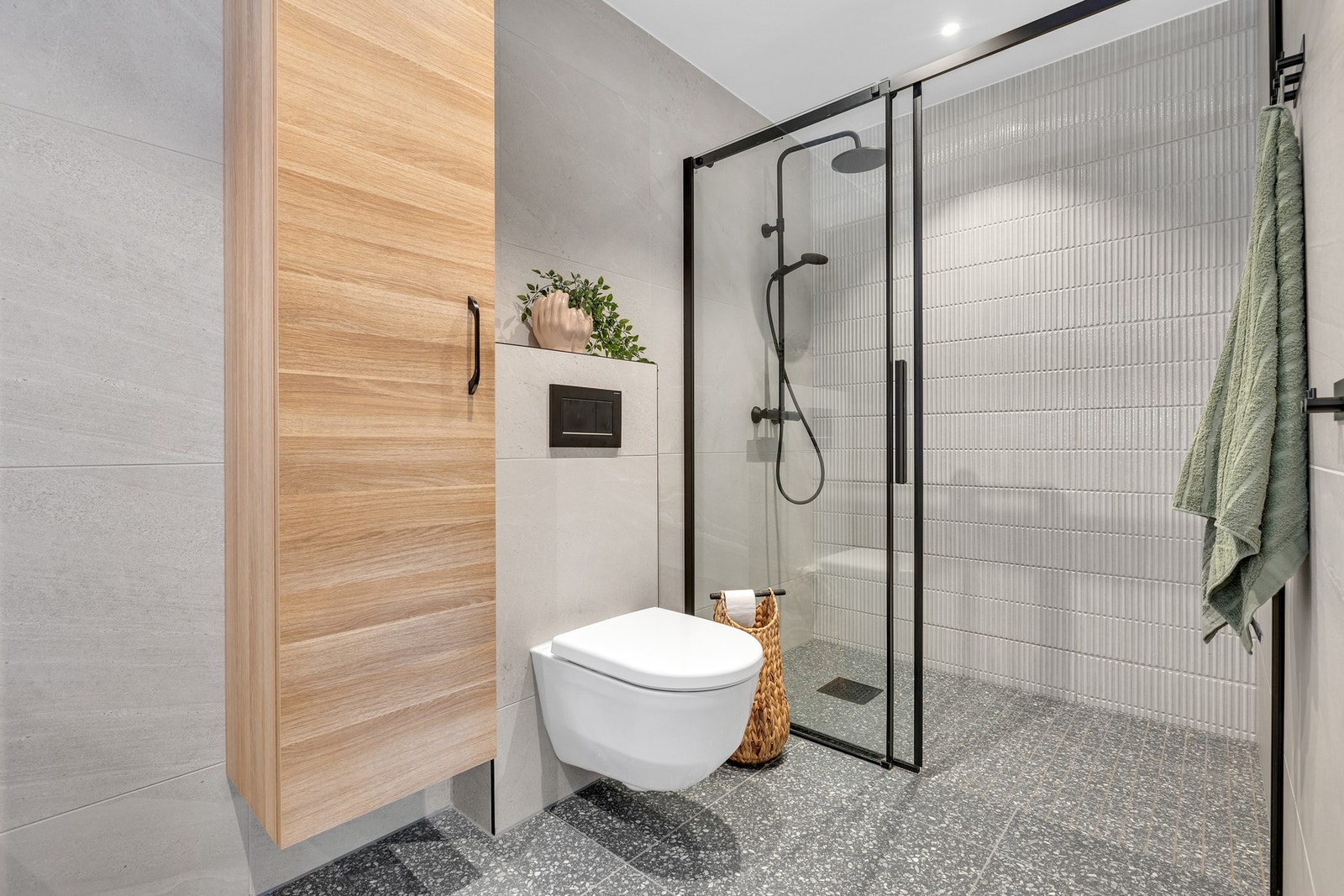 Vegghengt toalett og delikat dusjnisje med sort skyvedør og dusjgarnityr. Galleribilde