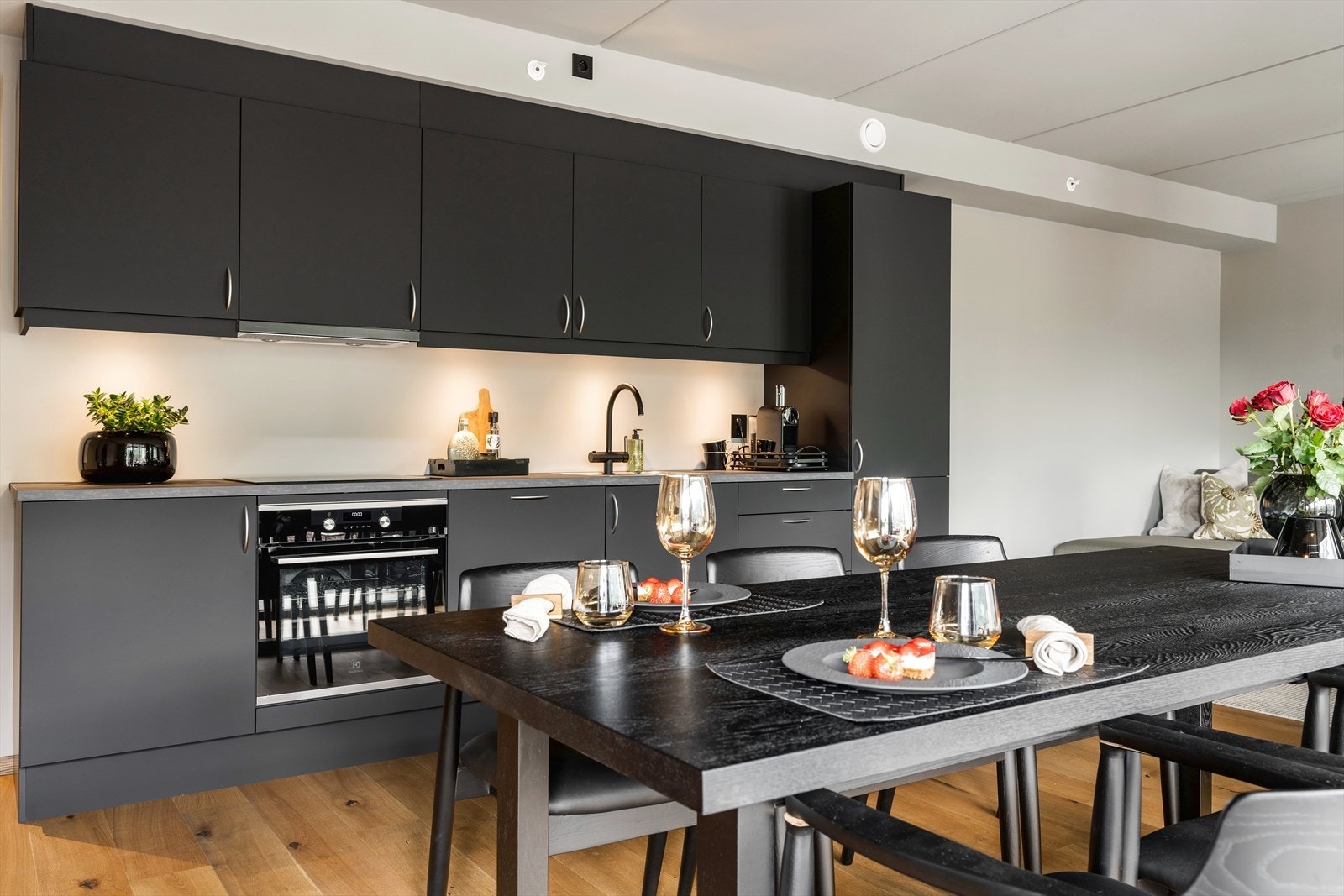 Moderne kjøkken i åpen løsning med stilrene, mørke fronter og integrerte hvitevarer. Perfekt for matlaging og sosiale sammenkomster. Galleribilde