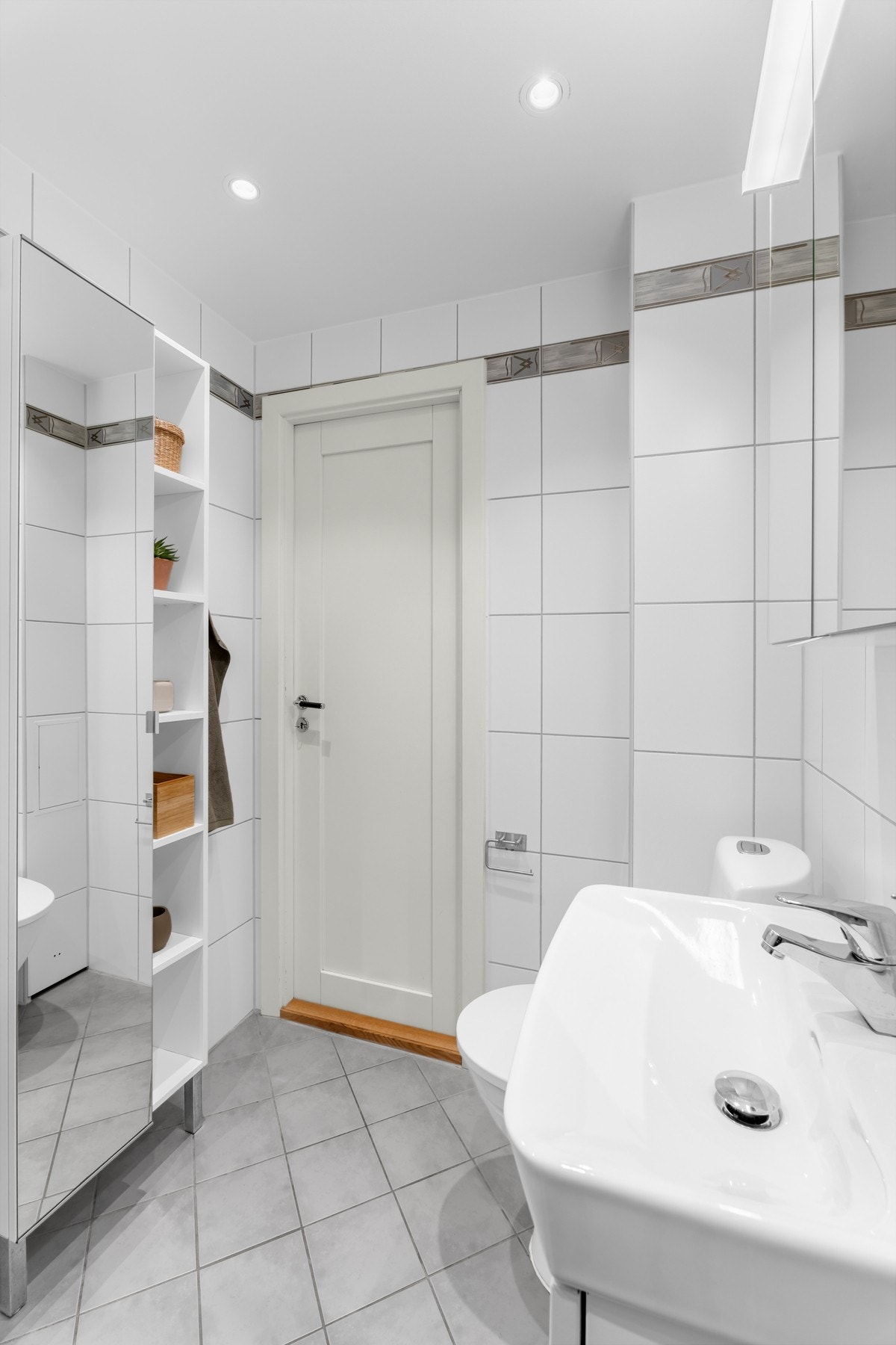Baderomsinnredningen har vegghengt servantskap med glatte fronter, heldekkende servant, speil med lys. Det er varmekabler i gulv og downlights i tak. Galleribilde