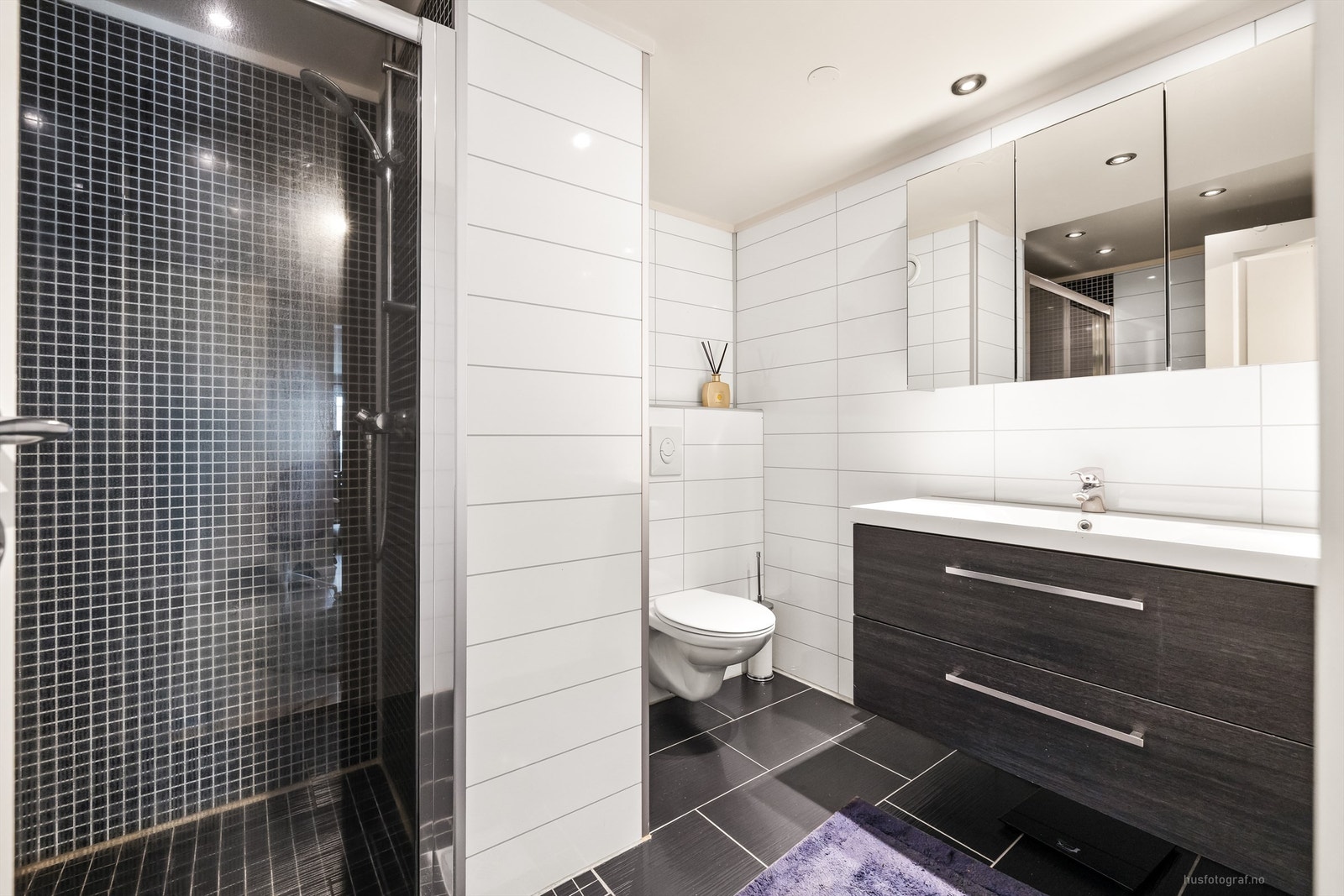 Badet har en romslig dusjnisje med skyvedørsramme av glass samt veggmontert dusjarmatur Galleribilde