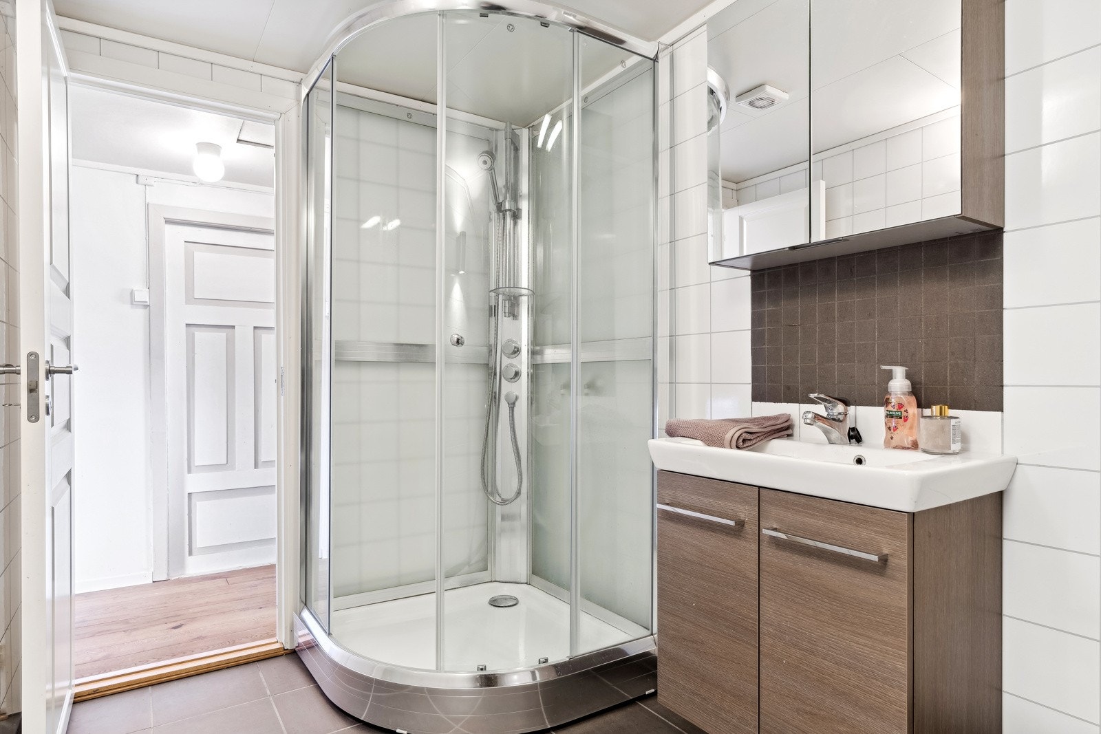 Bad utstyrt med dusjkabinett, speilskap med overlys og stikkontakt, servantinnredning og gulvstående toalett. Galleribilde