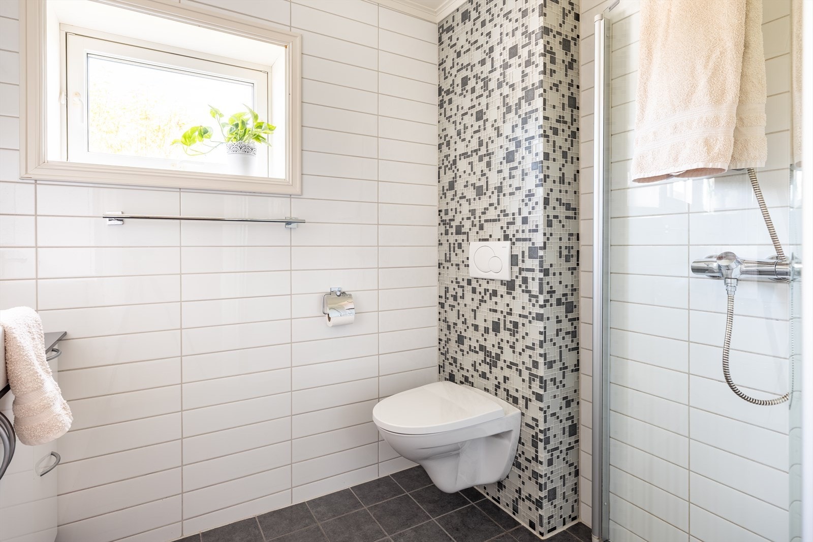 Badet er utstyrt med innfellbare dusjdører, mekanisk avtrekk, servant, servantskap og veggmontert wc. Galleribilde