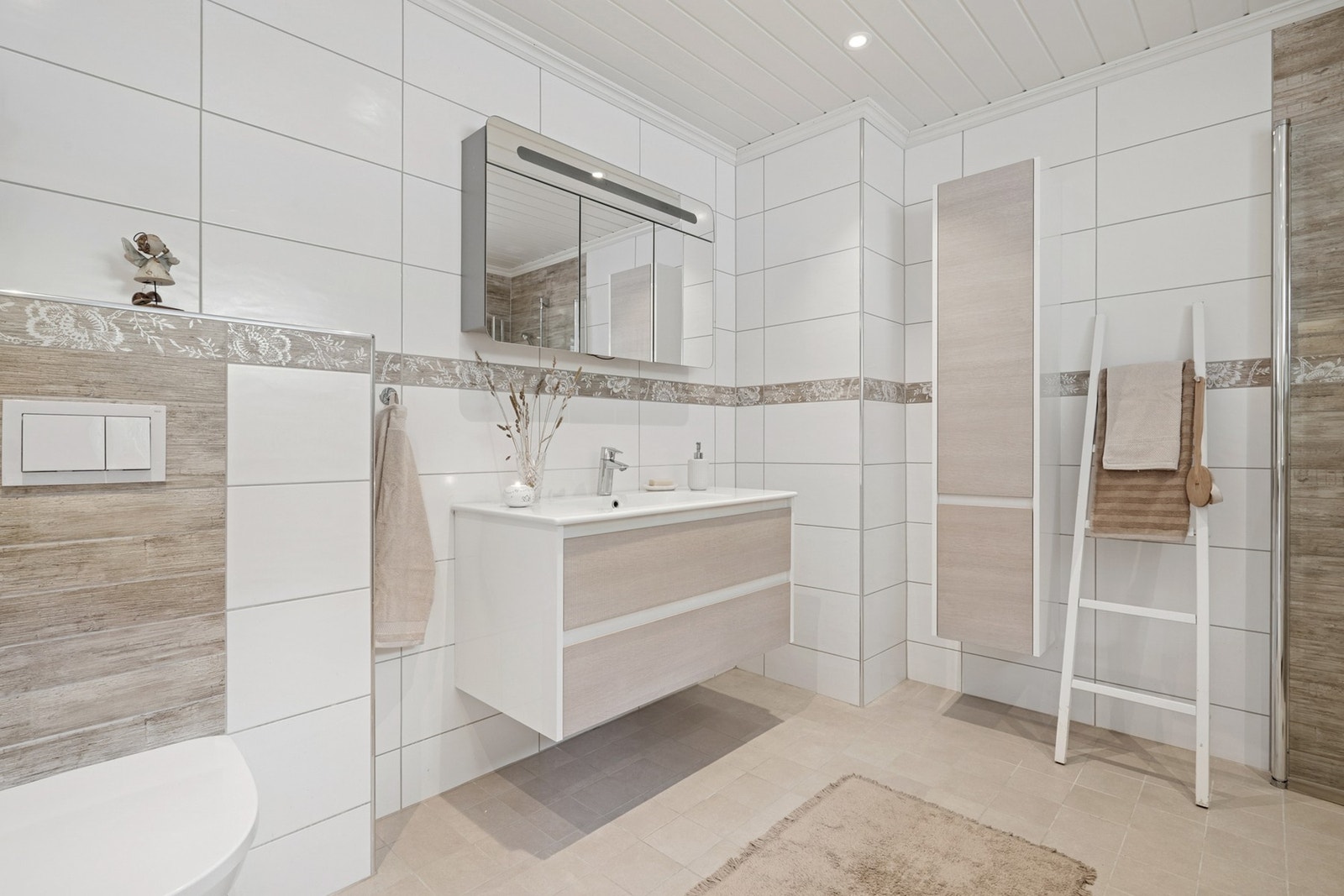 Badet er utstyrt med servantinnredning, speilskap, høyskap, vegghengt toalett og dusjhjørne med innfellbare dusjdører. Galleribilde