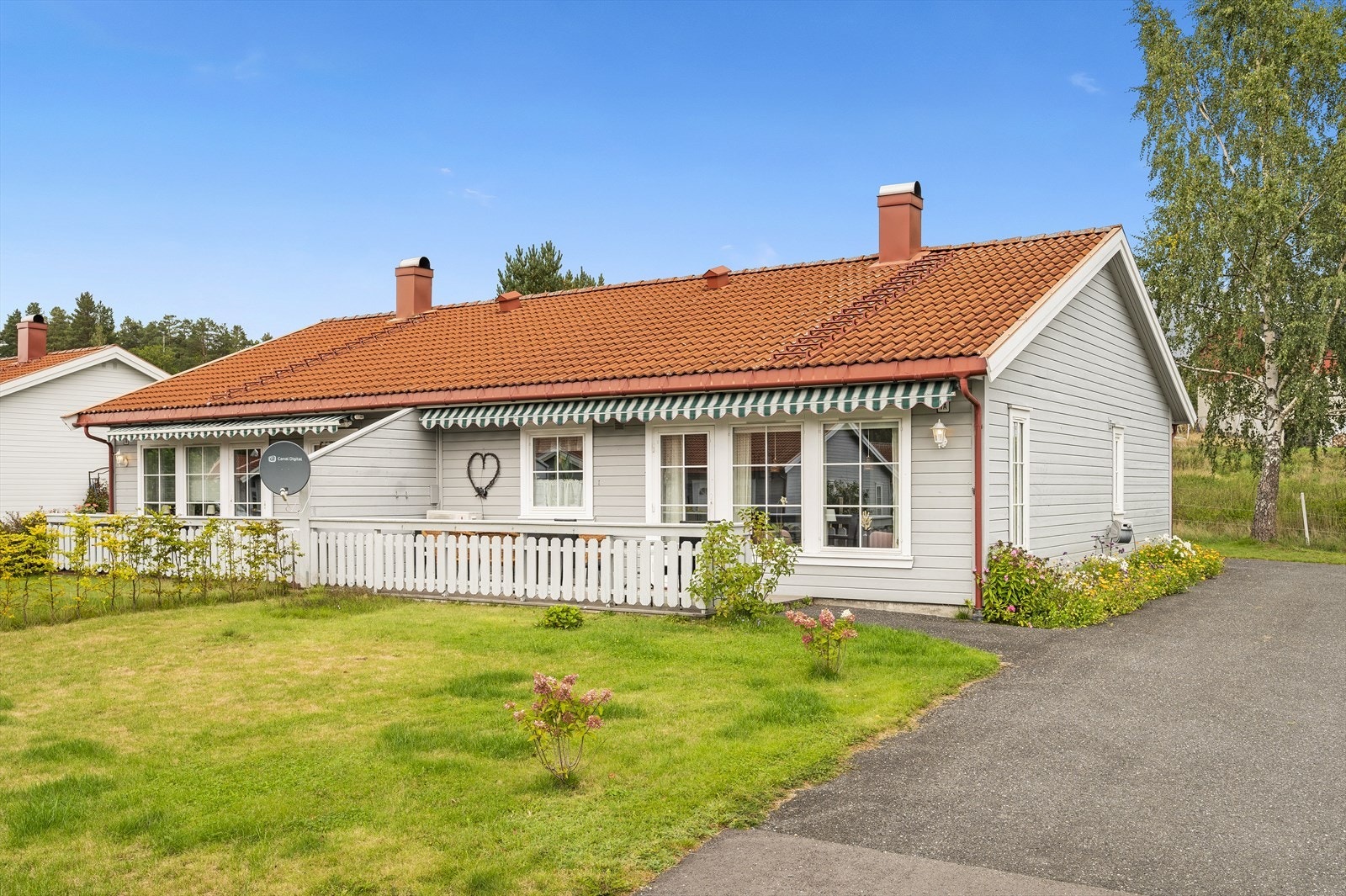Tomten fremstår med asfaltert adkomst, og ellers uteplass bestående av blomsterbed, gressplen og terrasse. Galleribilde