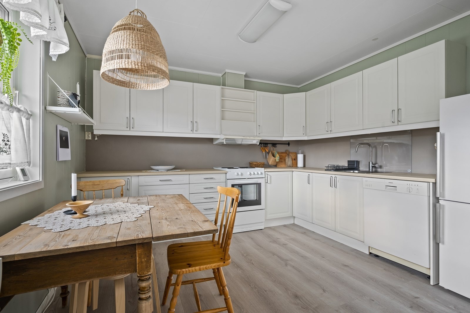 Kjøkkenet har en åpen løsning mot stuen, og består av en hvit, profilert innredning med laminert benkeplate. Galleribilde