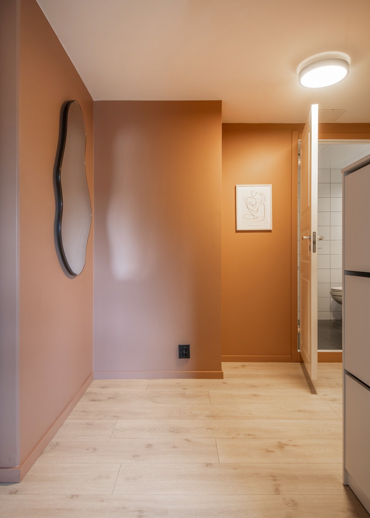 Veggene er malt i en varm, dempet terrakotta-/brunrosa nyanse, som gir rommet et behagelig uttrykk, mens gulvene er belagt med lyst laminat. Galleribilde