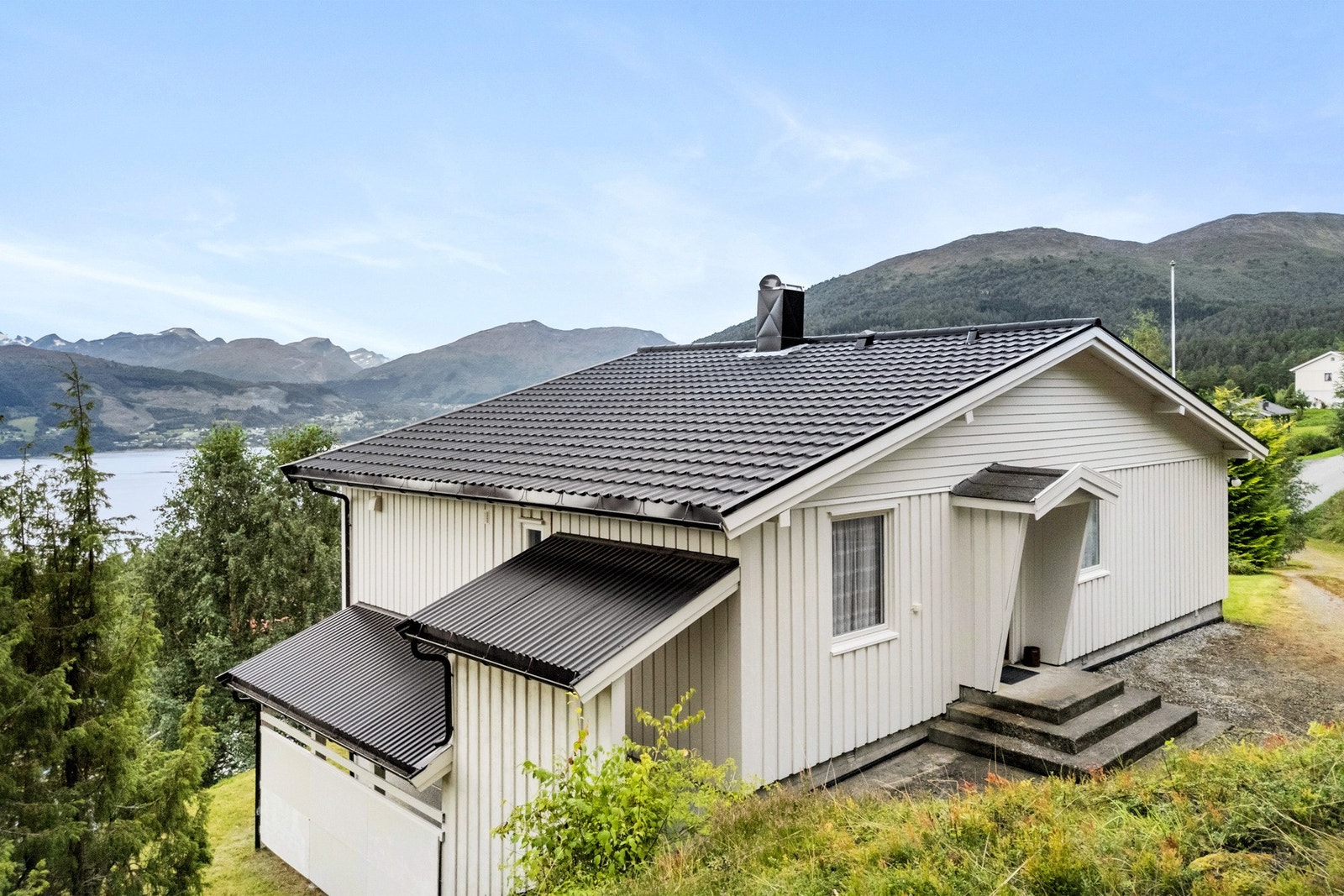 Du kan kjøre bilen helt til døra og det er veg i skrånende terreng opp til huset. Overbygd trappegang til sokkelleiligheten på østsiden. Galleribilde