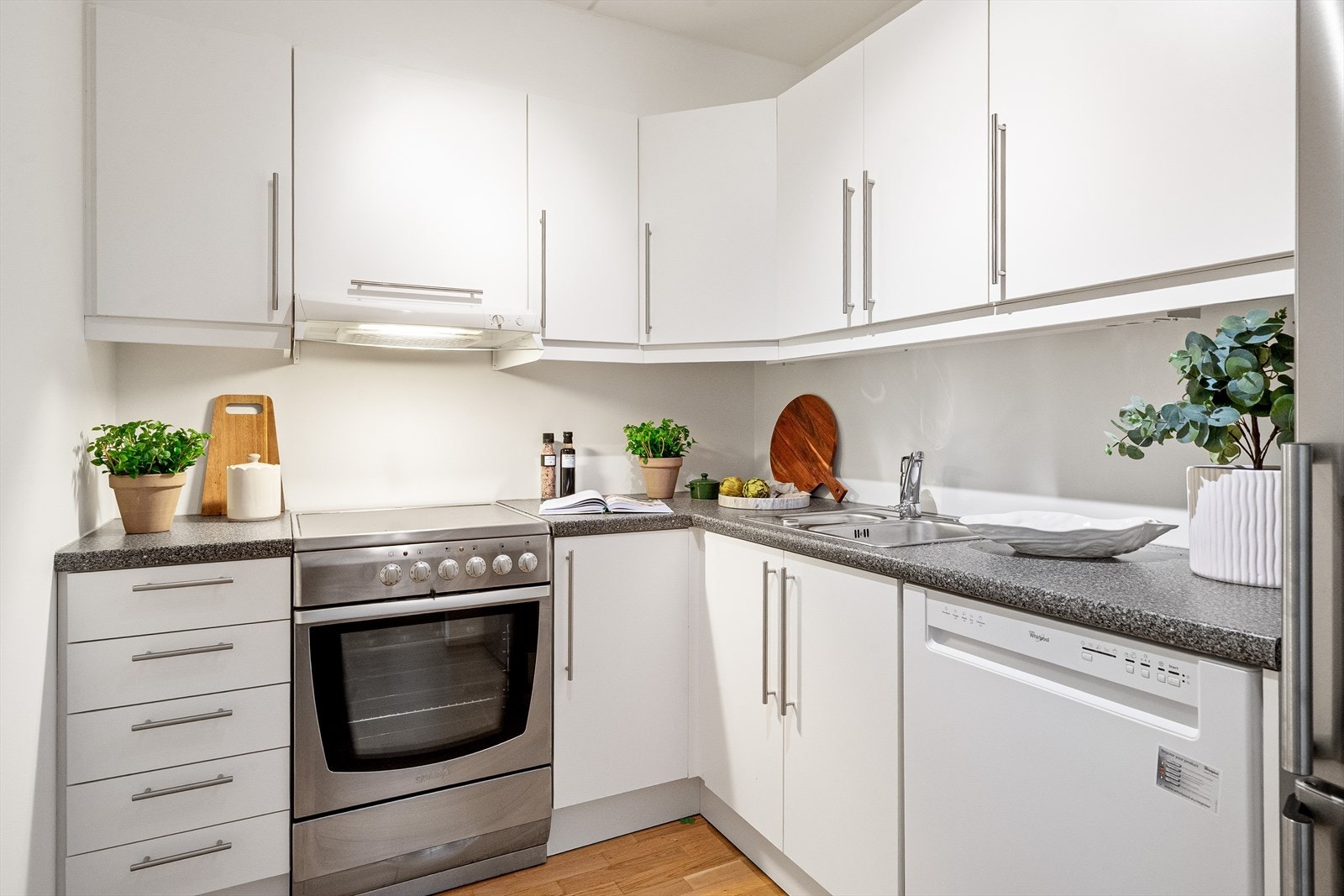 Lys innredning med glatte fronter og benkeplate i laminat. Dobbel oppvaskkum med svingbart blandebatteri fra Oras. Kjøkkenet har frittstående hvitevarer med oppvaskmaskin, kjøl/fryseskap og komfyr med platetopp. Galleribilde