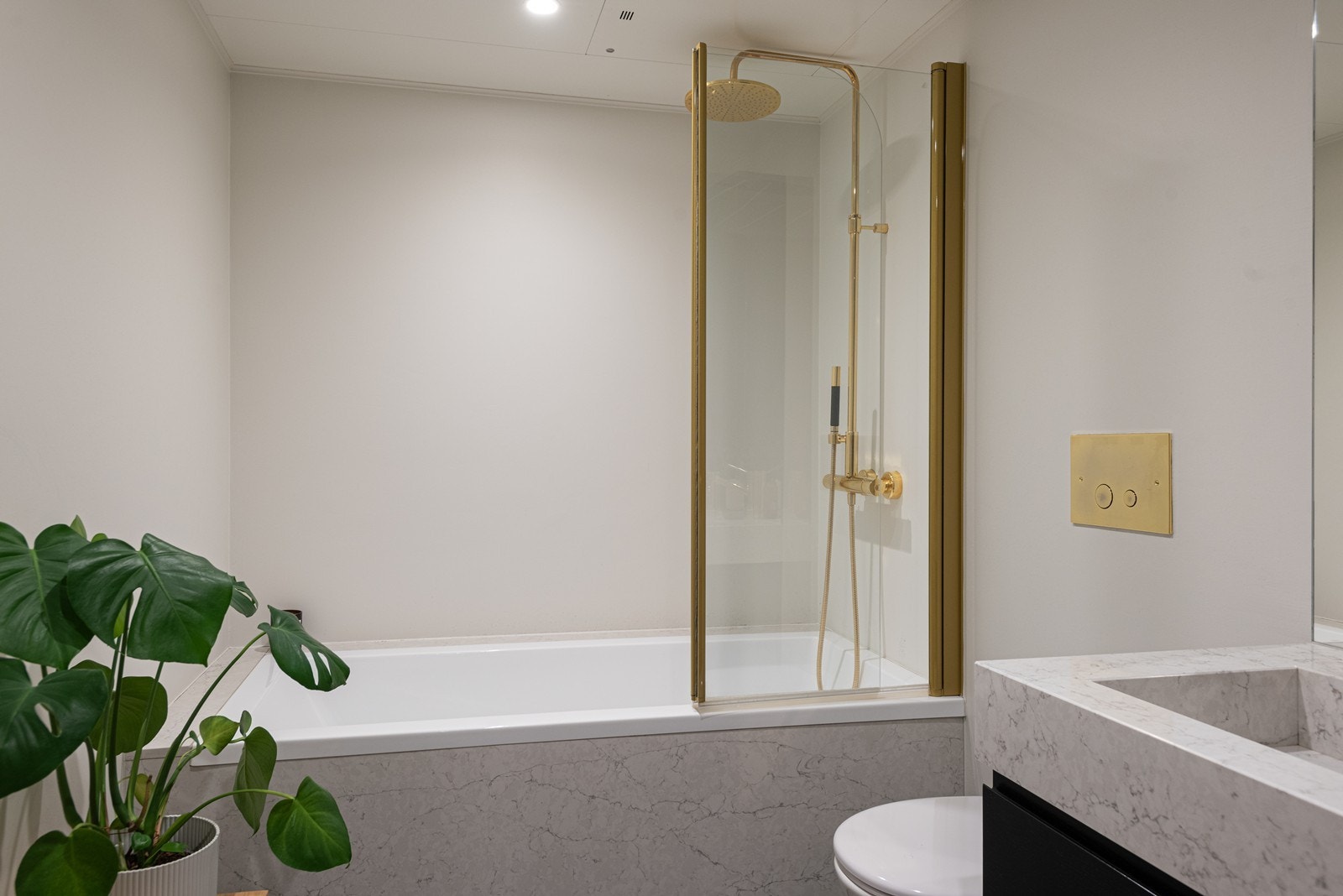 Badet har flislagt gulv og vegger kledd med våtromsplater. Det er innredet med vegghengt toalett, servant integrert i møbelinnredning samt badekar med glassvegg Galleribilde