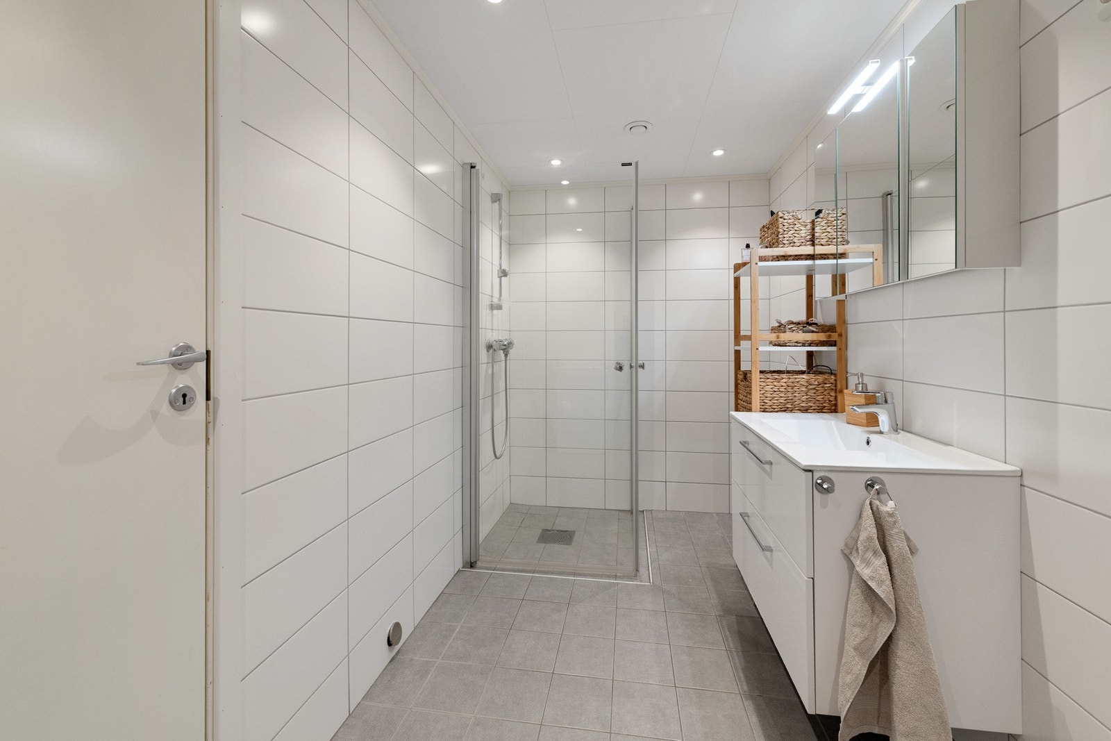 Baderomsinnredningen inkluderer praktiske elementer som dushjørne med glassvegger, vegghengt servantinnredning og et speilskap med belysning over servanten. Galleribilde