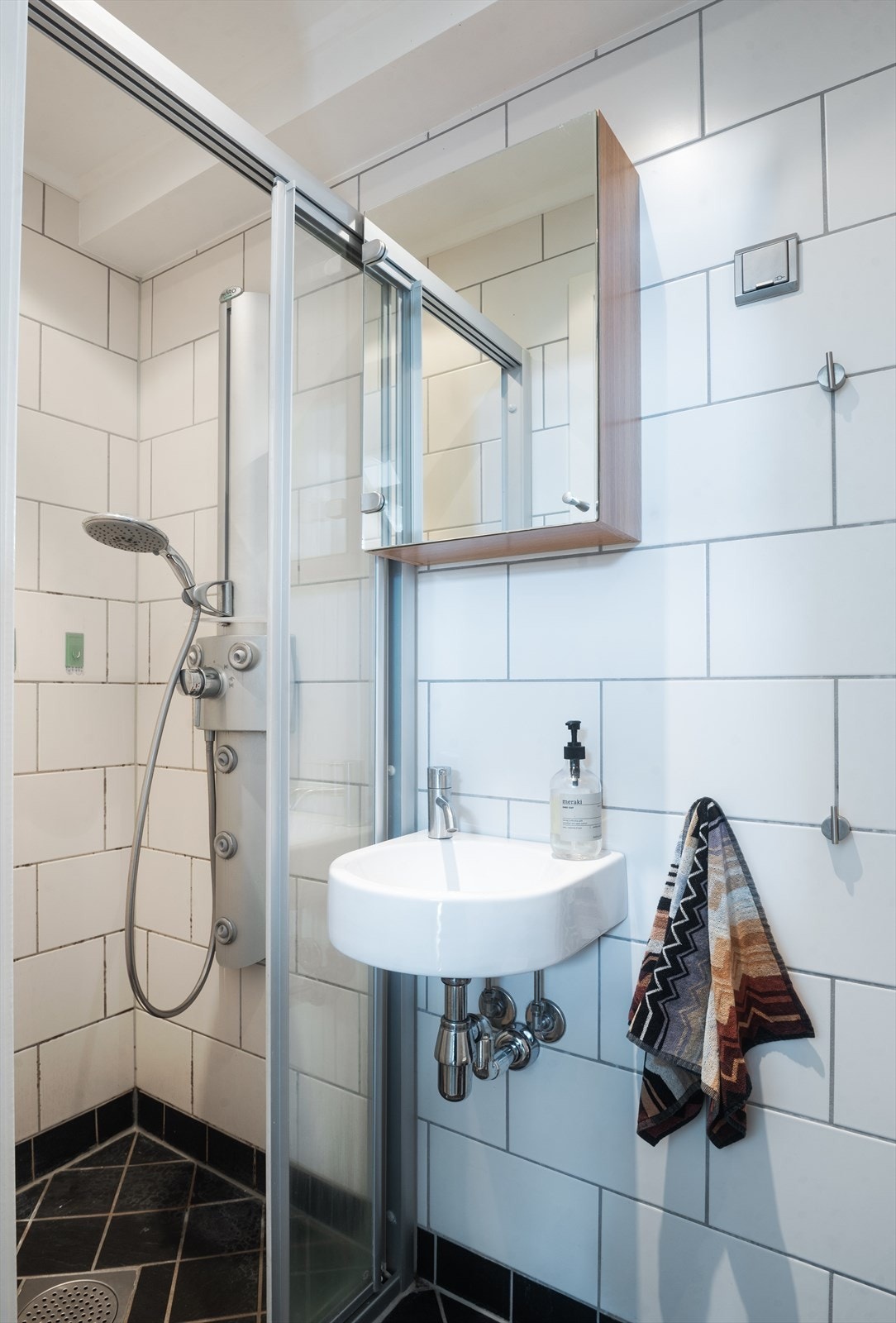 Flislagt baderom med vegghengt servant med ettgreps blandebatteri og overhengende speil, gulvstående toalett og skyve-dusjvegger. Galleribilde