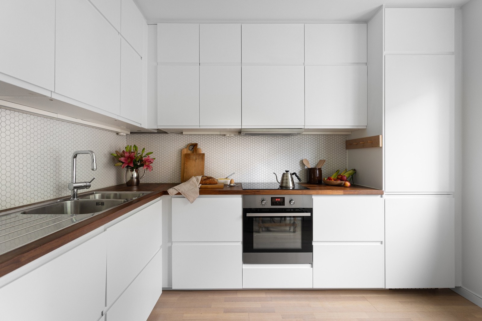 Moderne kjøkken fra 2015 med glatte hvite flater, integrerte hvitevarer og benkeplater i tre. Galleribilde