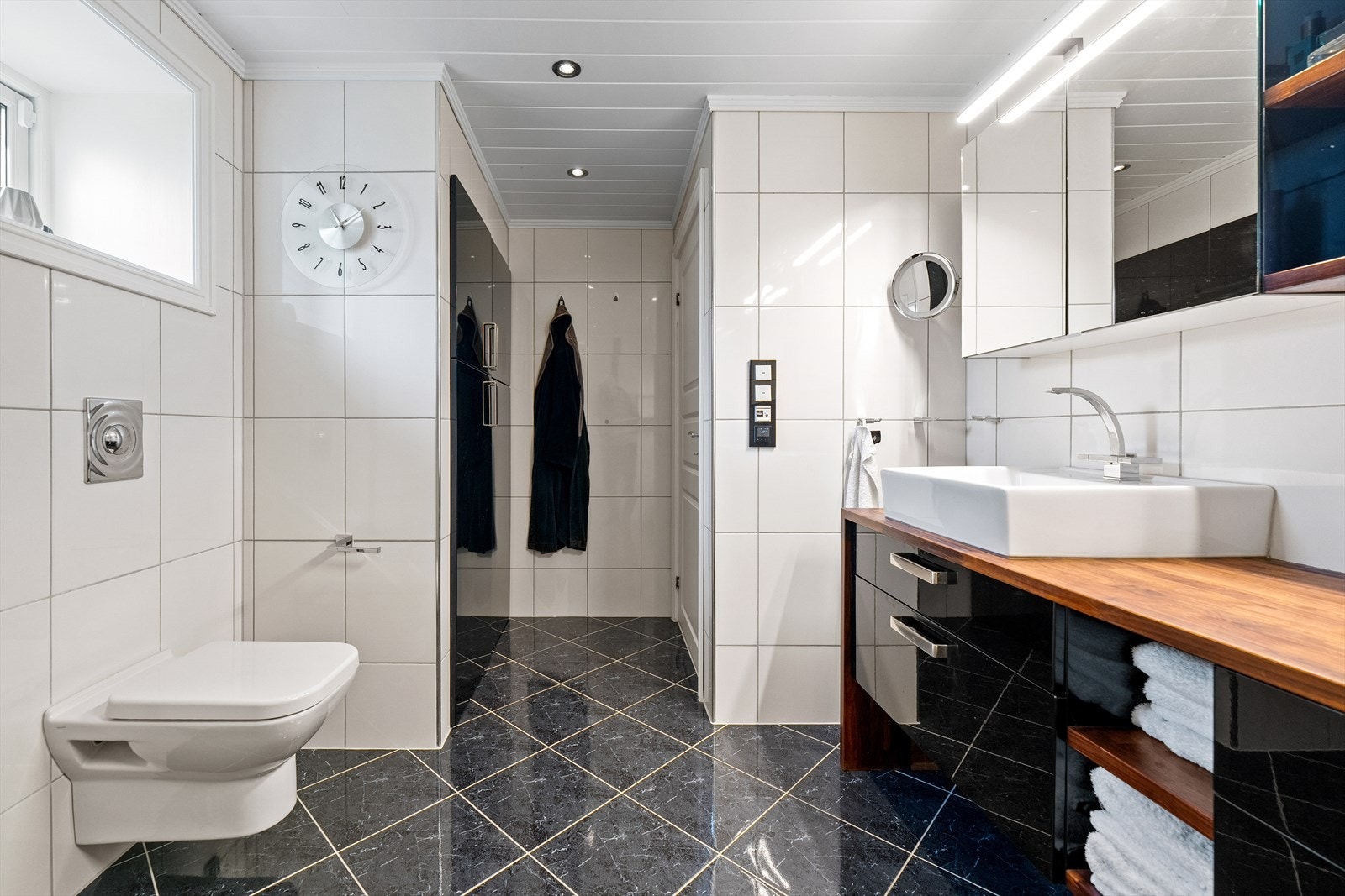 Innredningen har sorte høyglansfronter og benkeplate i valnøtt med to toppmonterte servanter. Det er også her laget en smartløsning hvor det sorte skapet skjuler varmtvannstanken, samt opplegg for vaskemaskin og tørketrommel Galleribilde