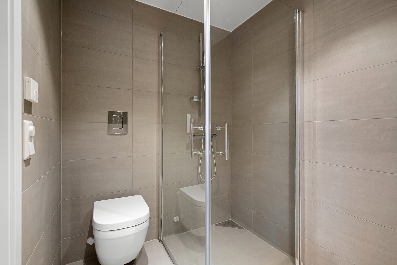 Badet inneholder vegghengt toalett, dusjsone med innfellbare dører samt servant armatur. Varme i gulv og downlightsbelysning i taket. Bilde fra leilighet G305 Galleribilde