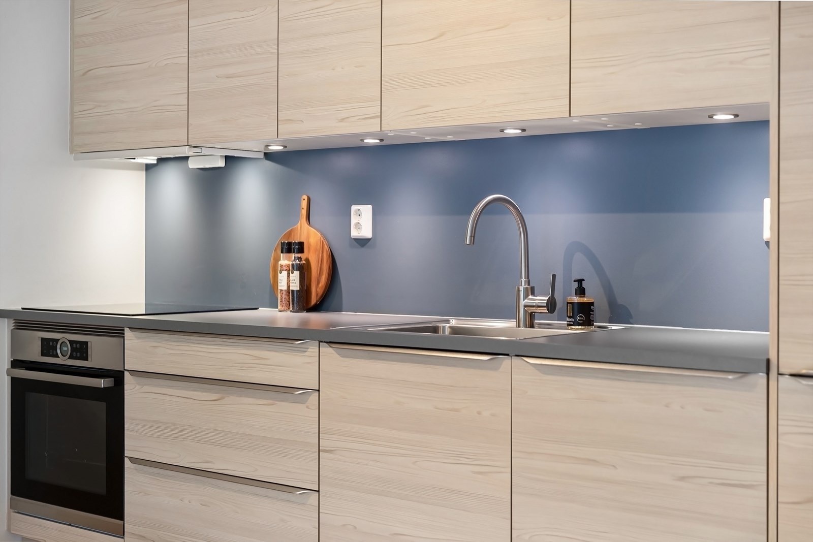 Kjøkkenet er innredet med glatte, moderne fronter og en slitesterk laminatbenkeplate med nedfelt kum i rustfritt stål. Praktisk belysning under overskapene og ventilator med avtrekk. Galleribilde