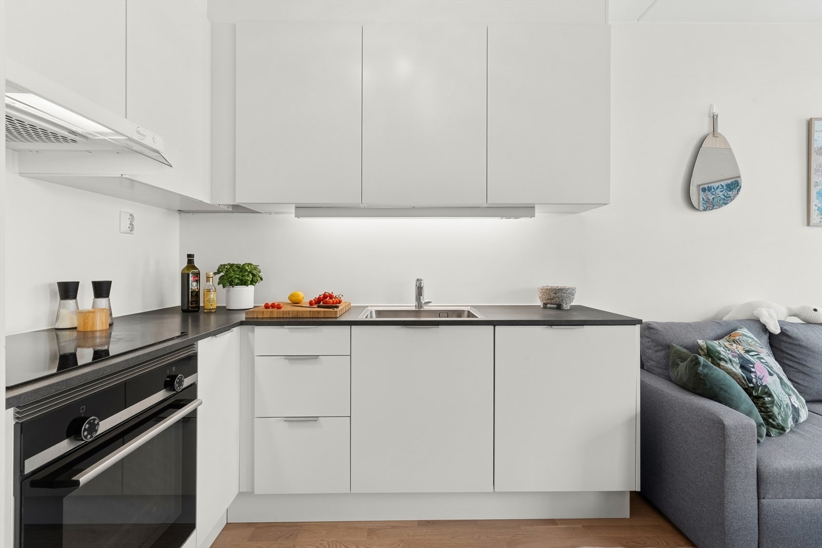 Kjøkkenet har glatte, fabrikklakkerte fronter og laminat benkeplate med nedfelt rustfri kum, kombinert med lysarmatur under overskap. Galleribilde