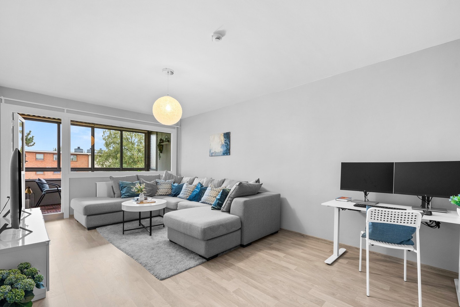 Store vindusflater fra 2023 slipper inn rikelig med dagslys, mens utgangen til en innglasset balkong gir en forlengelse av stuen. Galleribilde