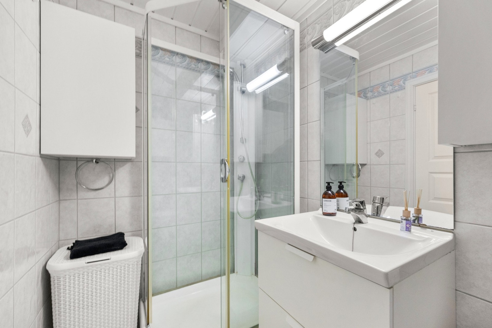 Baderomsinnredning med glatte, folierte fronter og heldekkende servant. Dusjkabinett med rette skyvedører og dusjutstyr. Galleribilde