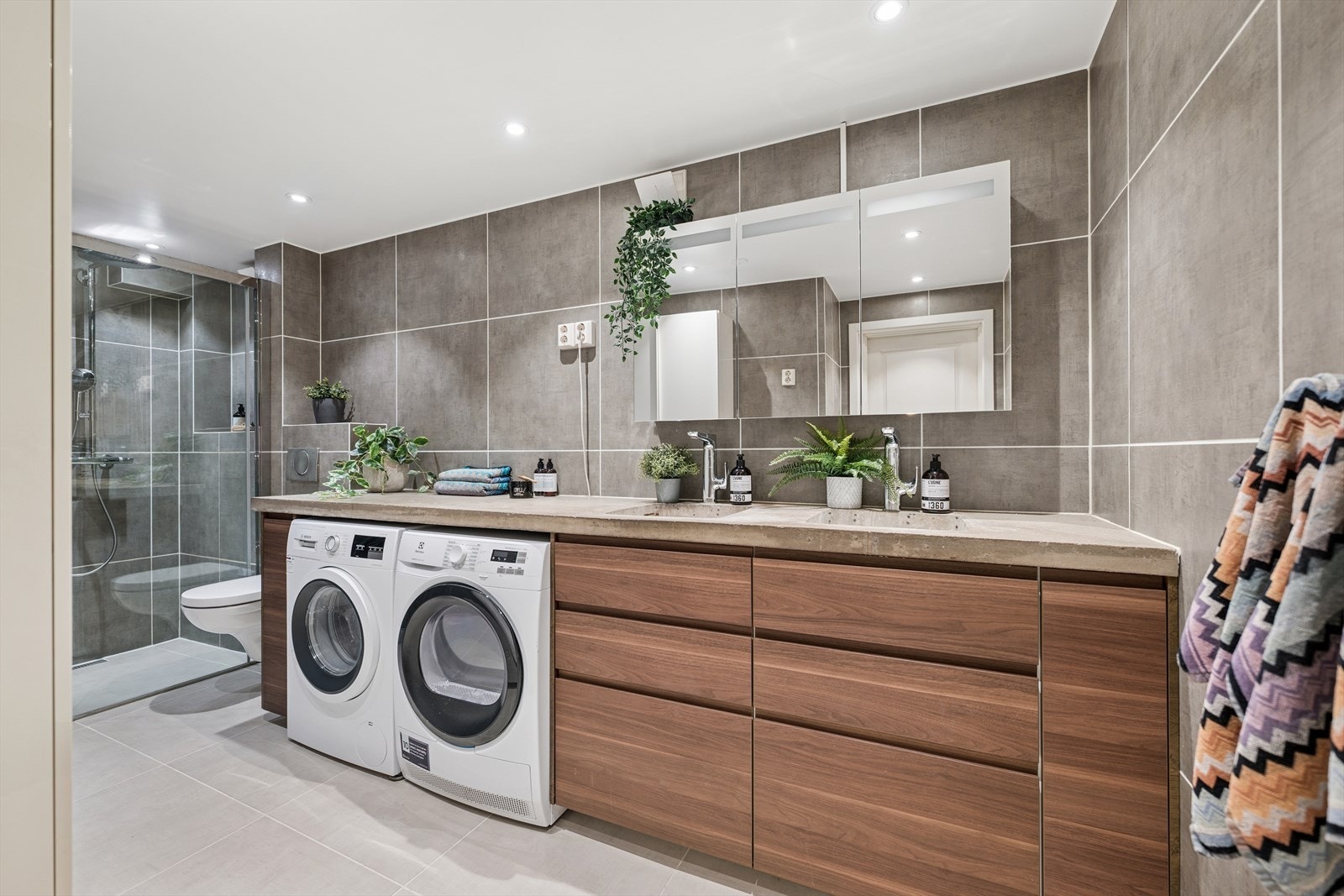 Baderommet fremstår som meget romslig og moderne. Det er flislagt med varmekabler i gulv og downlights i taket. Flisvalget er enkelt, delikat og behagelig samtidig som det er stilrent og moderne. Benkeplaten er i samme utførelse som kjøkkenet. Galleribilde