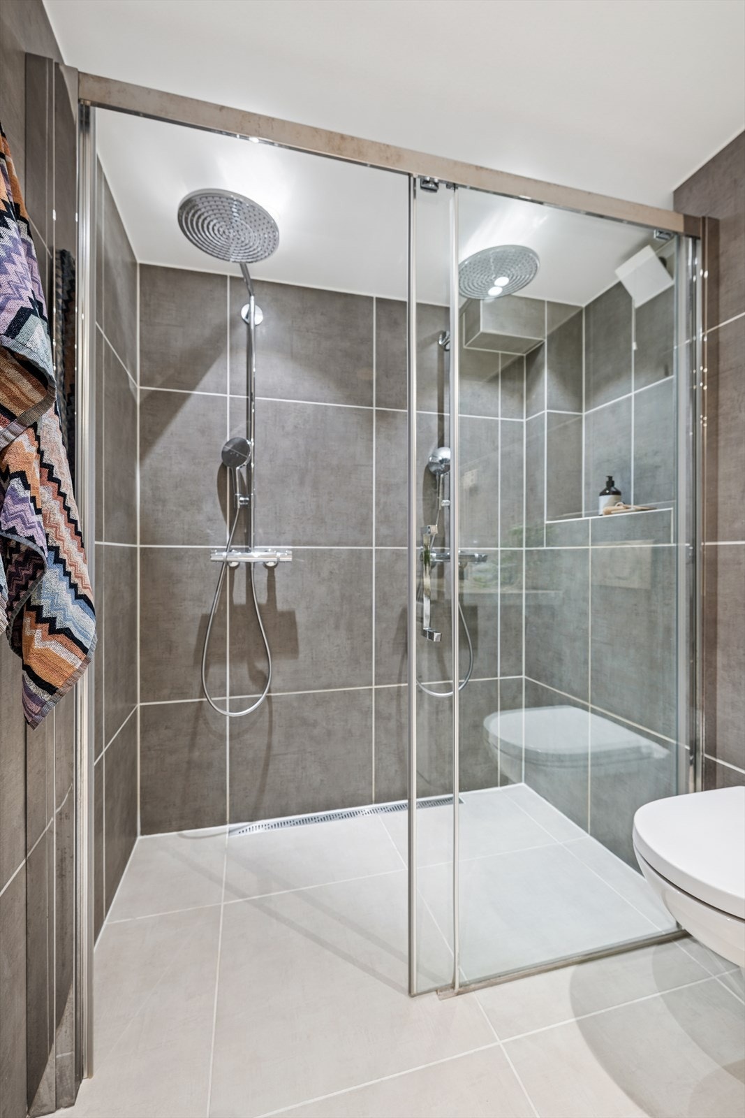 Badet har en stor dobbeltdusj med skyvedør. I dusj-sonen er det installert termostatstyrte dusjbatteriet. Sluket er i oval form og er formet i plast/stål. I tillegg er det en liten nisje for oppbevaring av dusjartikler. Galleribilde