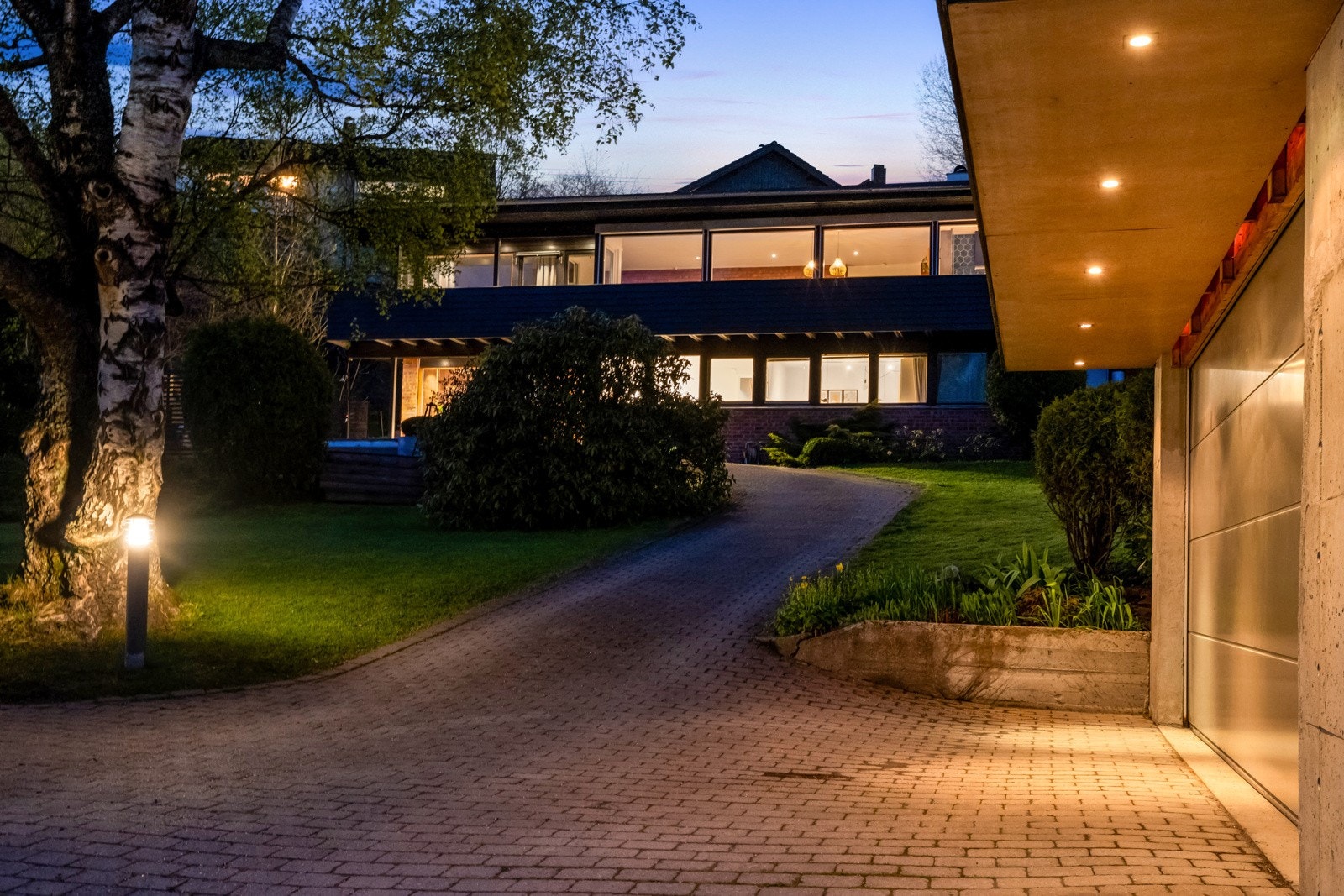 Oppkjørselen er pent opparbeidet med belegningsstein. Dobbelgarasjen er oppført i funkisstil i likhet med huset. Galleribilde