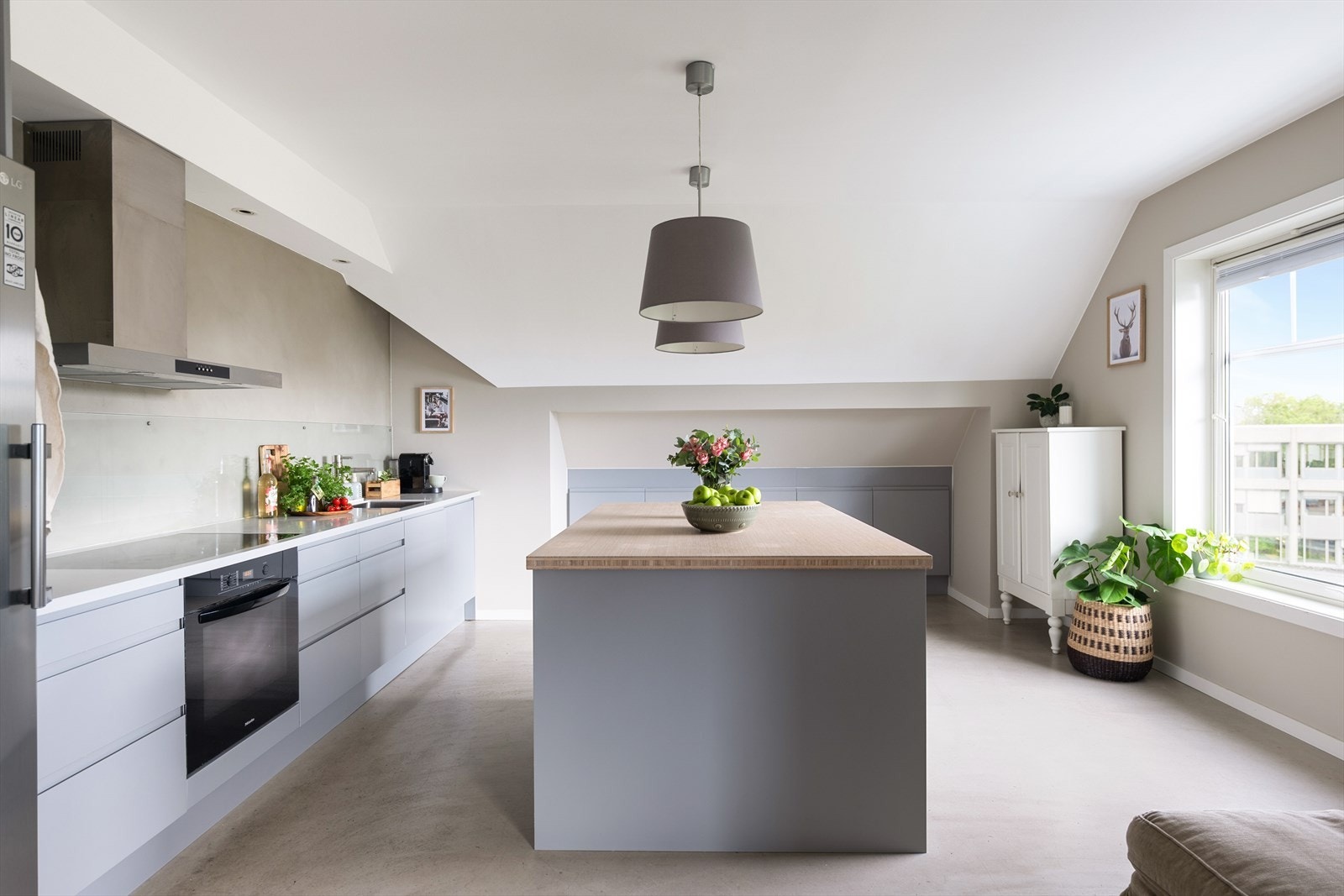 Boligens kjøkken er moderne med glatte, lakkerte skapfronter og en elegant benkeplate i stein med underlimt oppvaskkum. Galleribilde