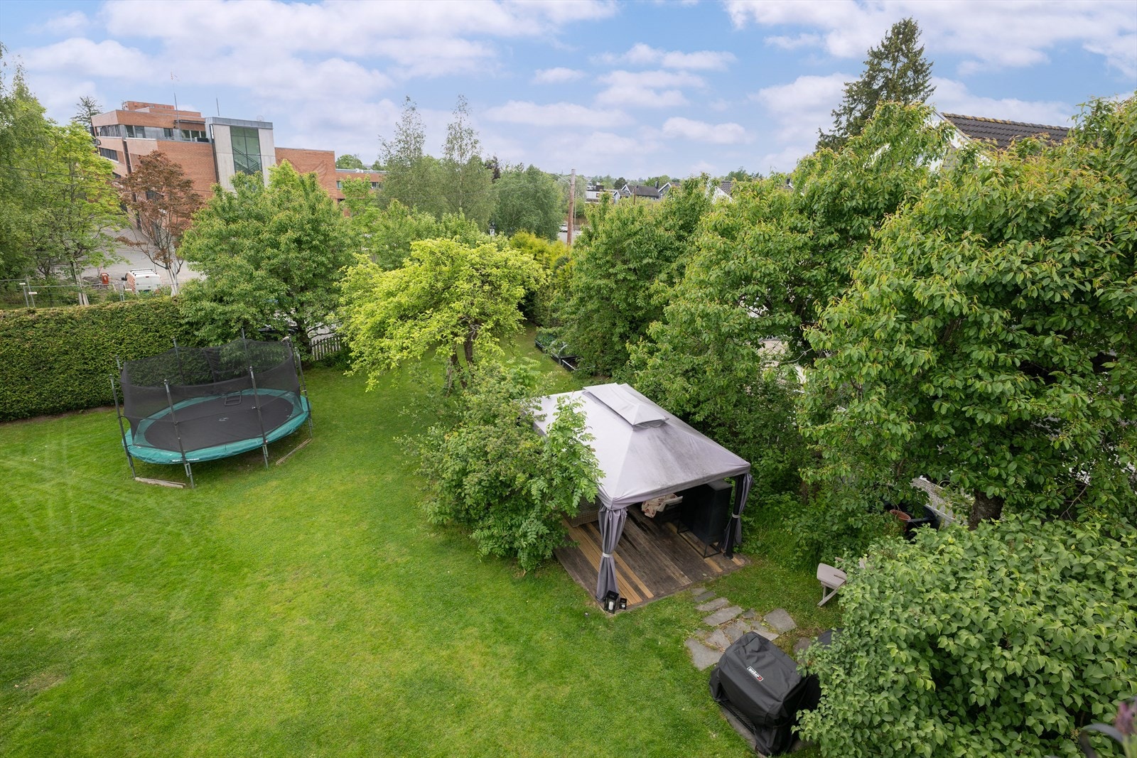 Fritt utsyn over den skjermede hagen, omgitt av grøntområder med busker og trær. Galleribilde
