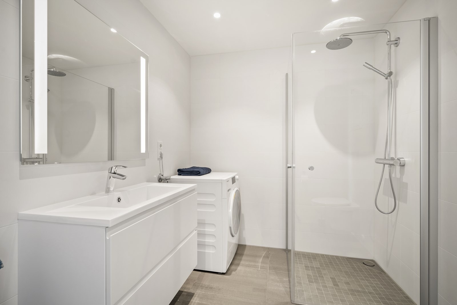 Badet er flislagt med store fliser i en elegant gråtone på gulvet og rene, hvite overflater som skaper en følelse av romslighet og god atmosfære. Galleribilde