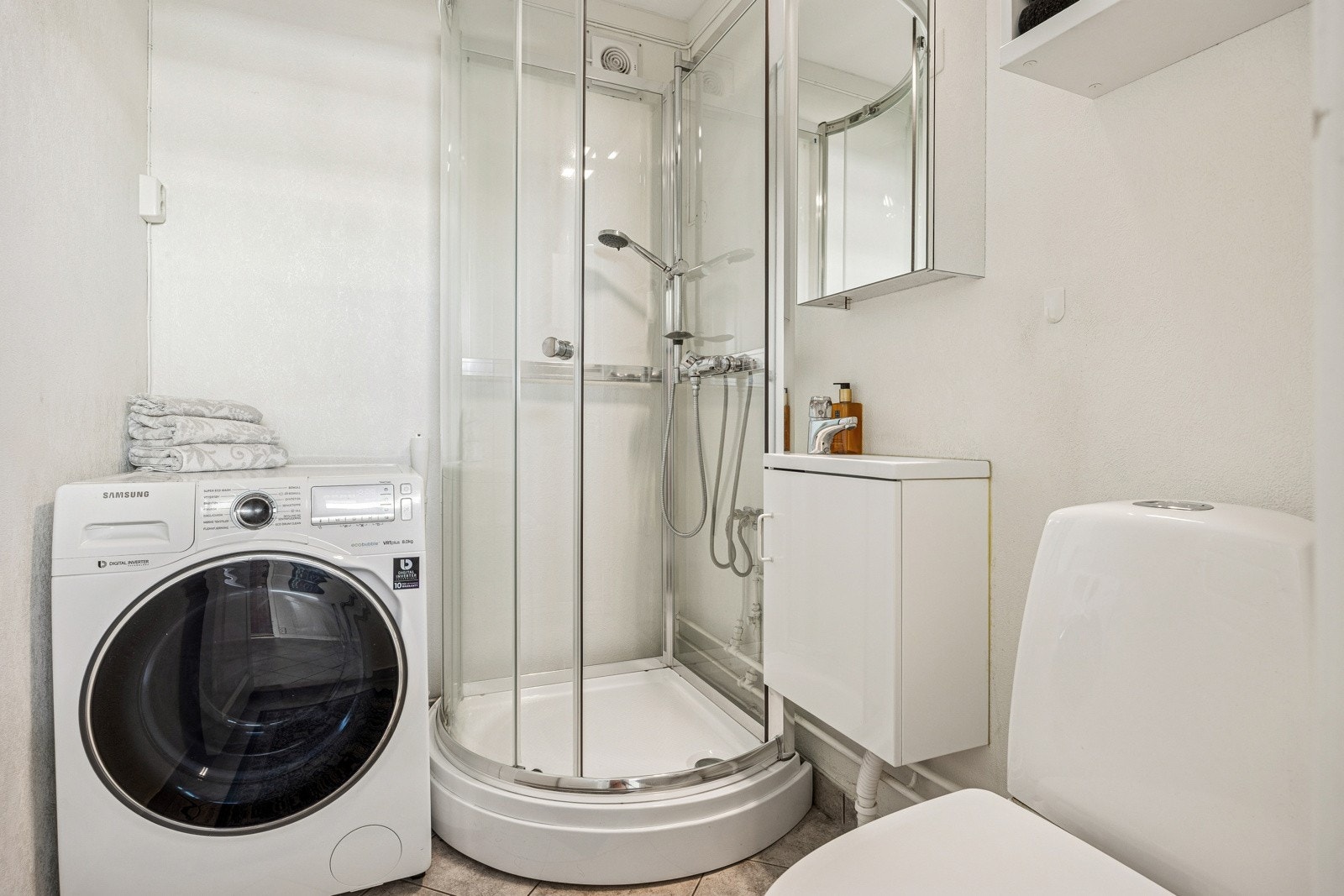 Vegg i vegg med entréen har man et praktisk bad/vaskerom, med toalett, dusjkabinett, opplegg for vaskemaskin, samt en enkel innredning med servantskap og speilskap. Galleribilde