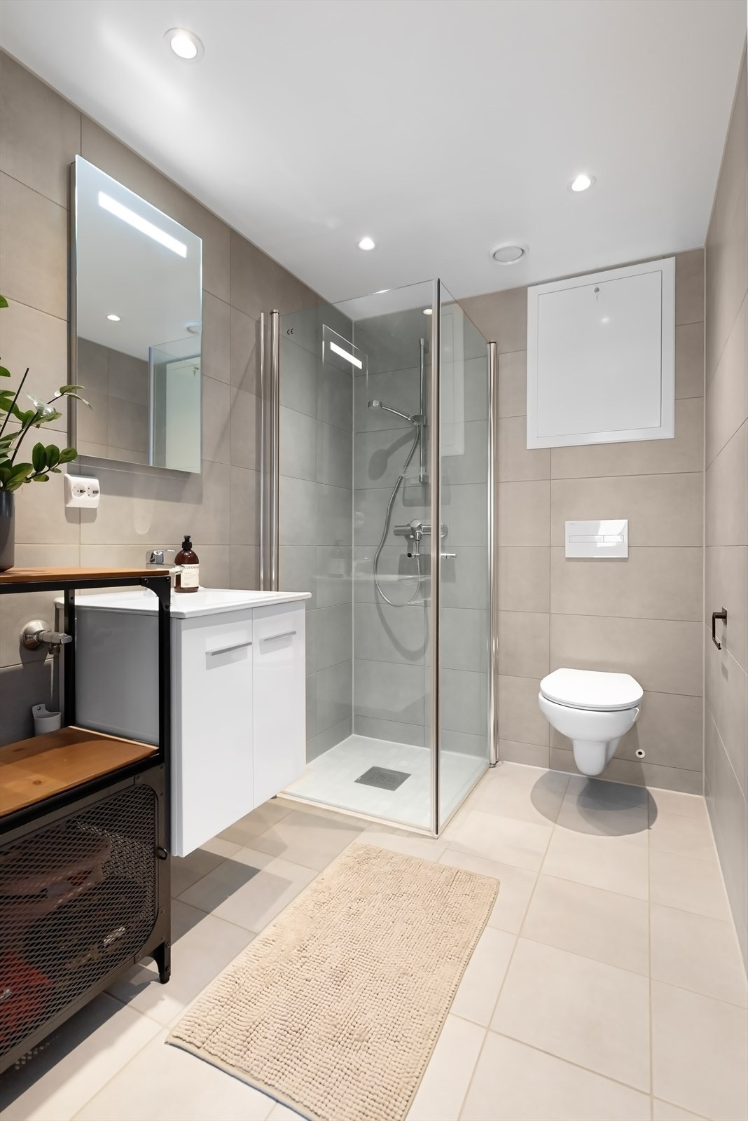 Innredet med hjørnedusj, servant med skuffer, ledspeil og veggmontert toalett. Galleribilde