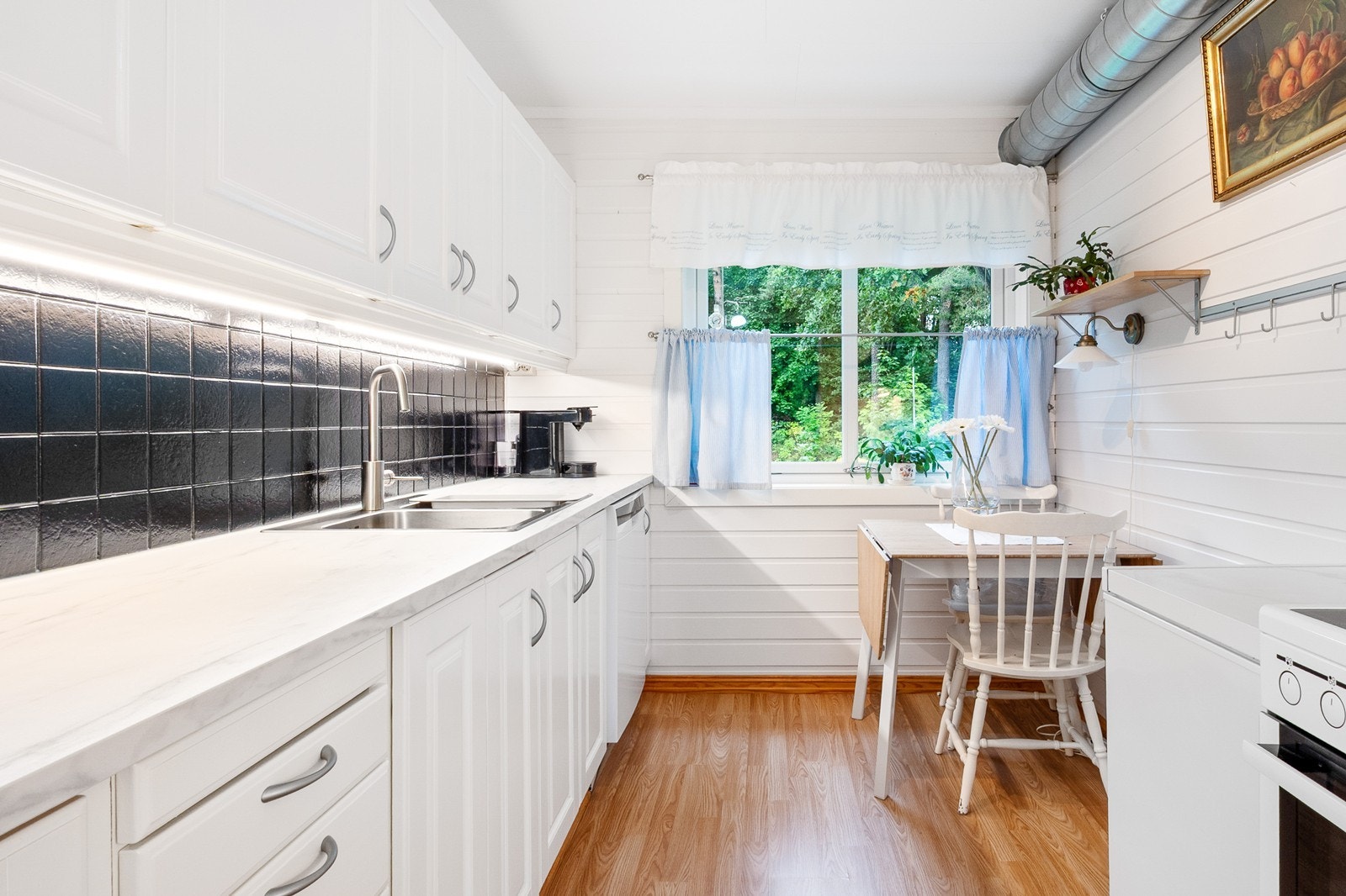 Innredningen har hvite, profilerte fronter, benkeplate i laminat og fliser over benk. Ny kjøkkenventilator, oppvaskmaskin, komfyr, oppvaskkum, blandebatteri og benkeplate 2019. Galleribilde