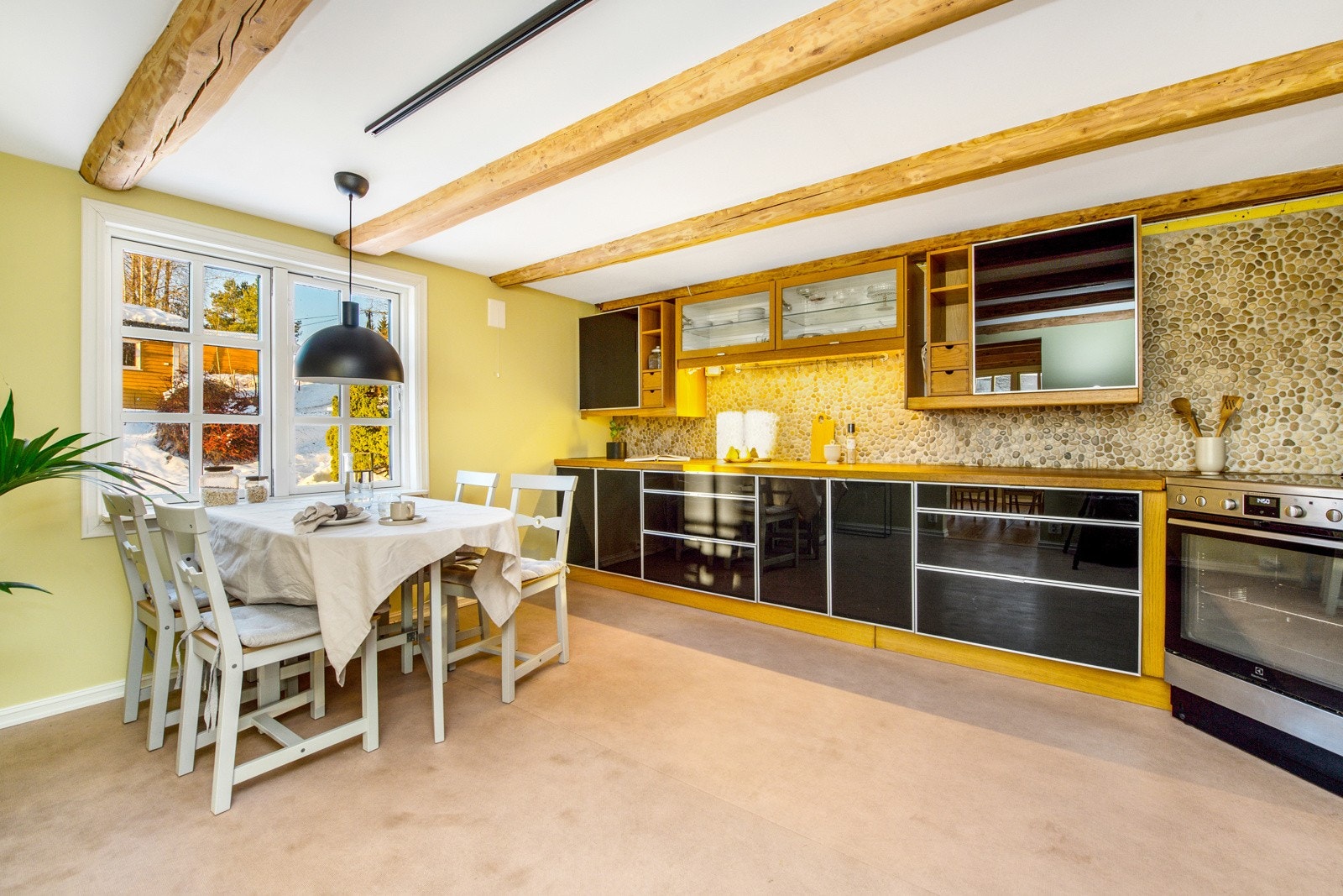 Innenfor spisestuen har boligen et stort kjøkken med gulvbelegg, synlige takbjelker og vegger malt i en lys grønnfarge. Galleribilde