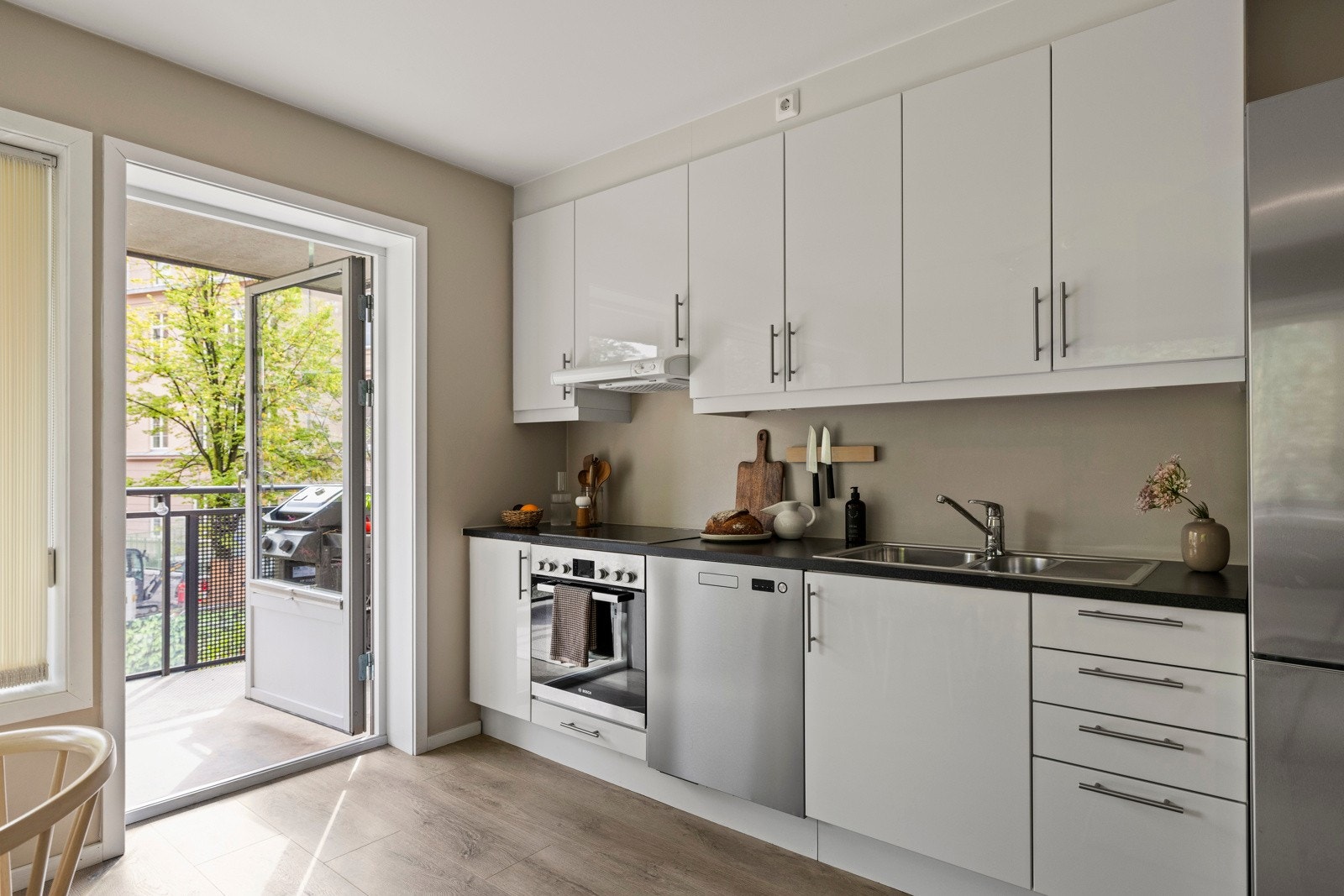 Hvite fronter og mørk benkeplate gir et tidløst uttrykk. Her har du godt med benkeplass, integrerte hvitevarer og praktiske løsninger for matlaging i hverdagen Galleribilde