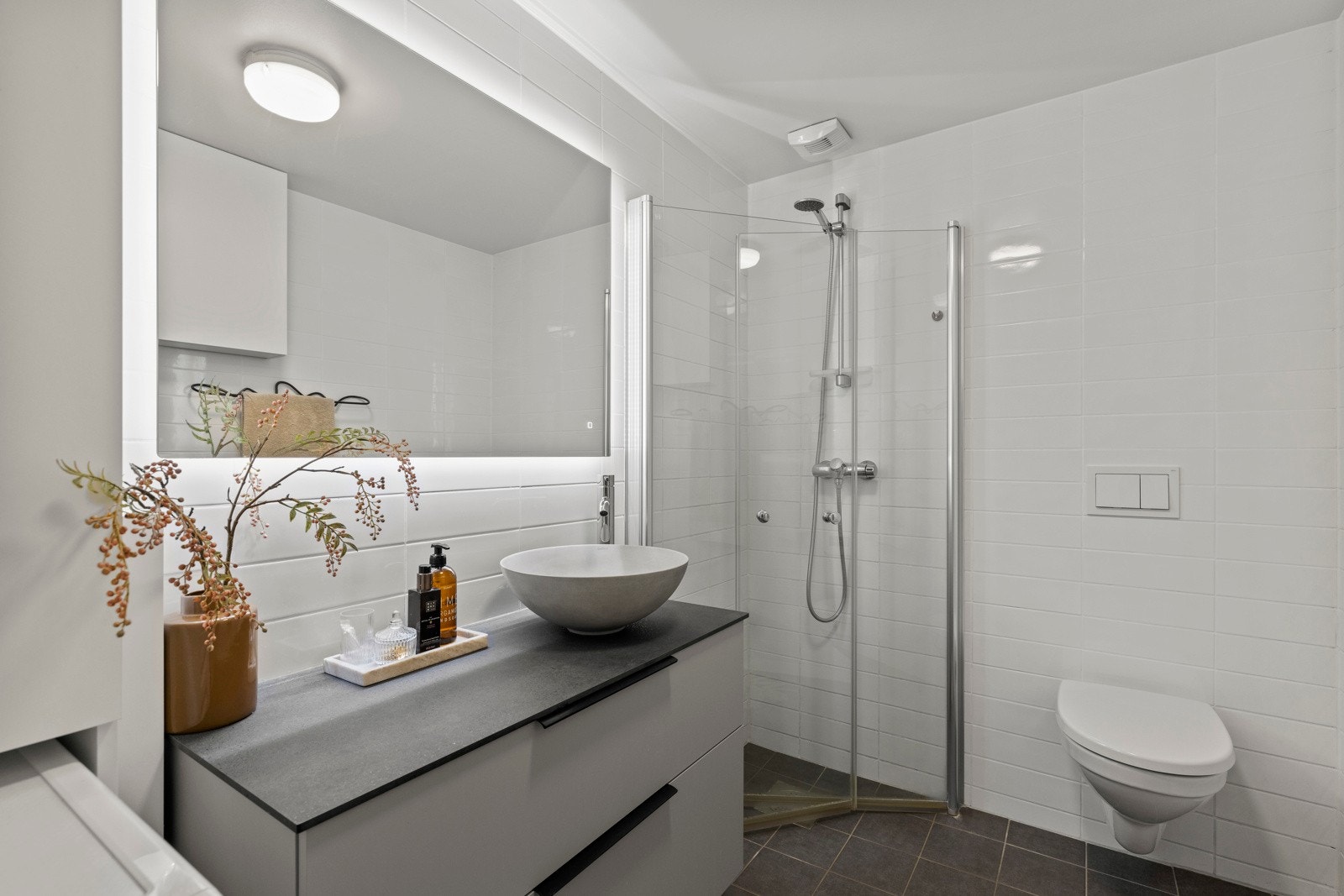 Rommet er utstyrt med dusjhjørne med glassdører, vegghengt toalett, servant med underskap og speil med belysning. Galleribilde