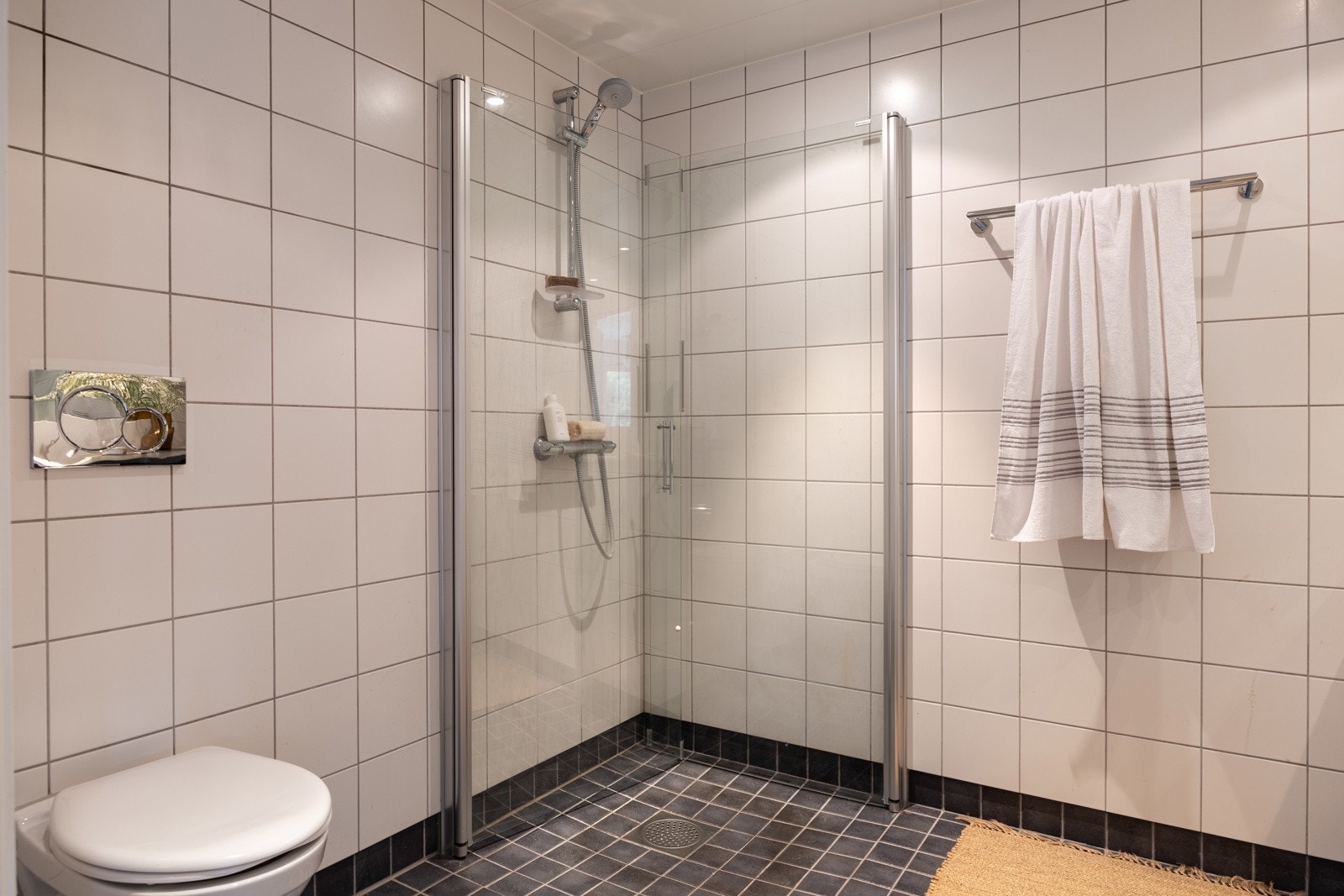 Rommet er innredet med dusjhjørne i herdet glass, servant med skapinnredning, speil og vegghengt toalett. Galleribilde