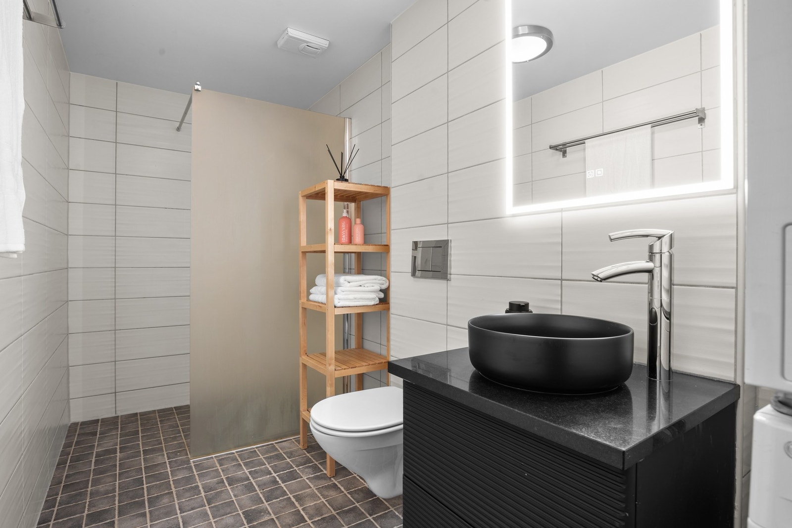 Romslig flislagt bad med vegghengt toalett, dusjhjørne, moderne servant og baderomsinnredning, samt speil med lyskilde Galleribilde